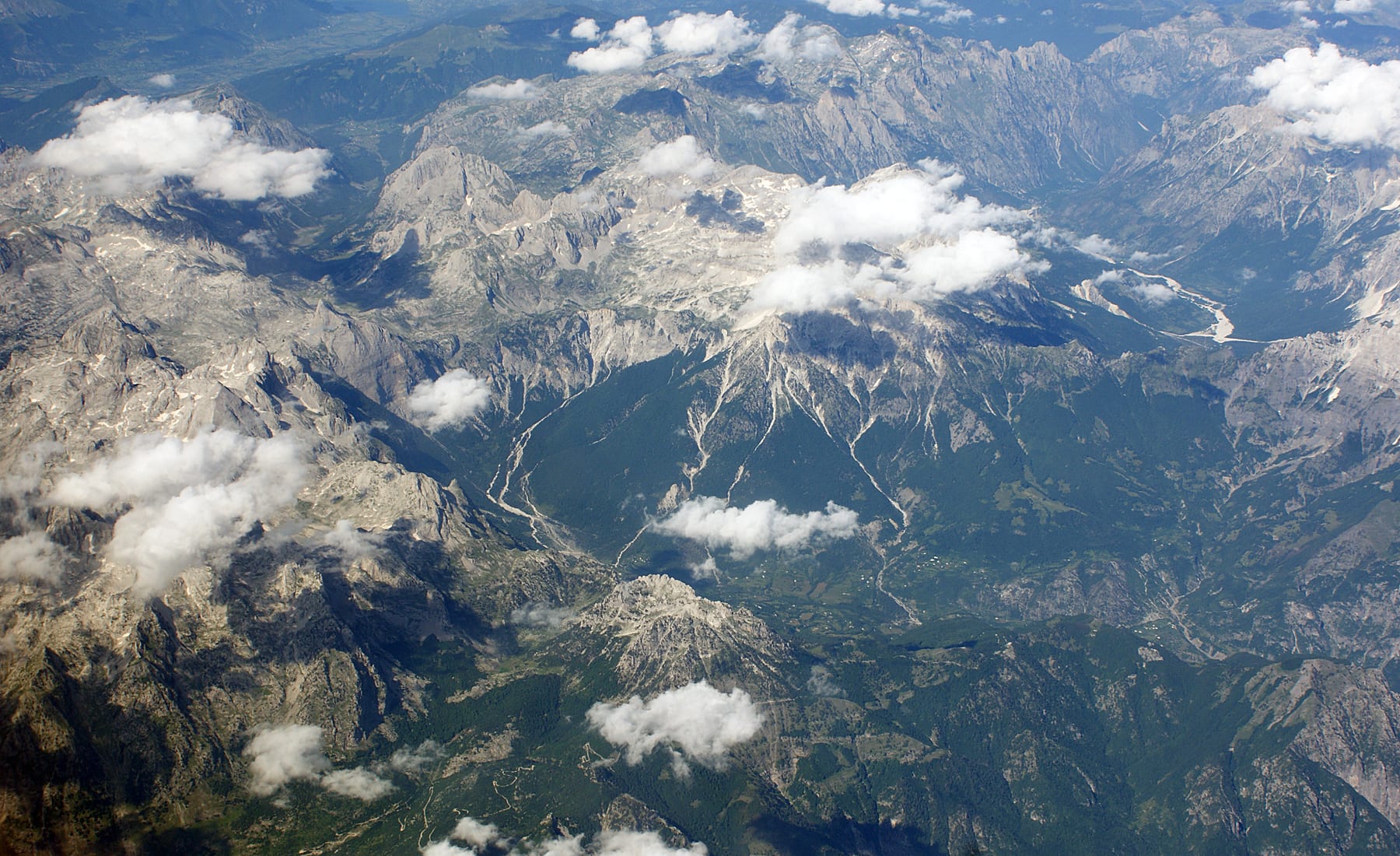 Aerial view of the jagged grey peaks of the Albanian Alps, with the green valley and village of Theth in the centre
