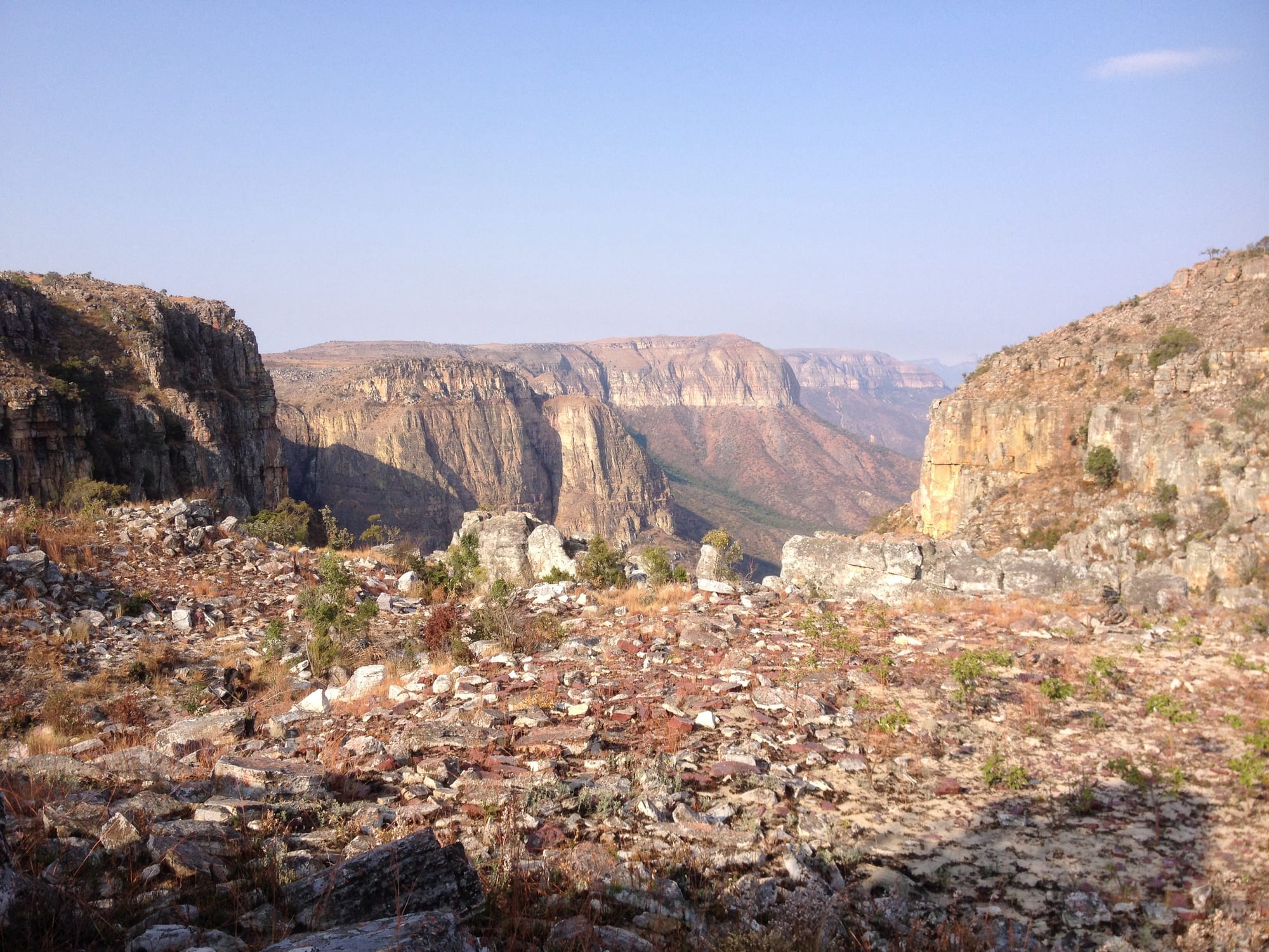 A rocky plateau edge looking out between sandstone cliffs into a deep canyon and hazy escarpments beyond
