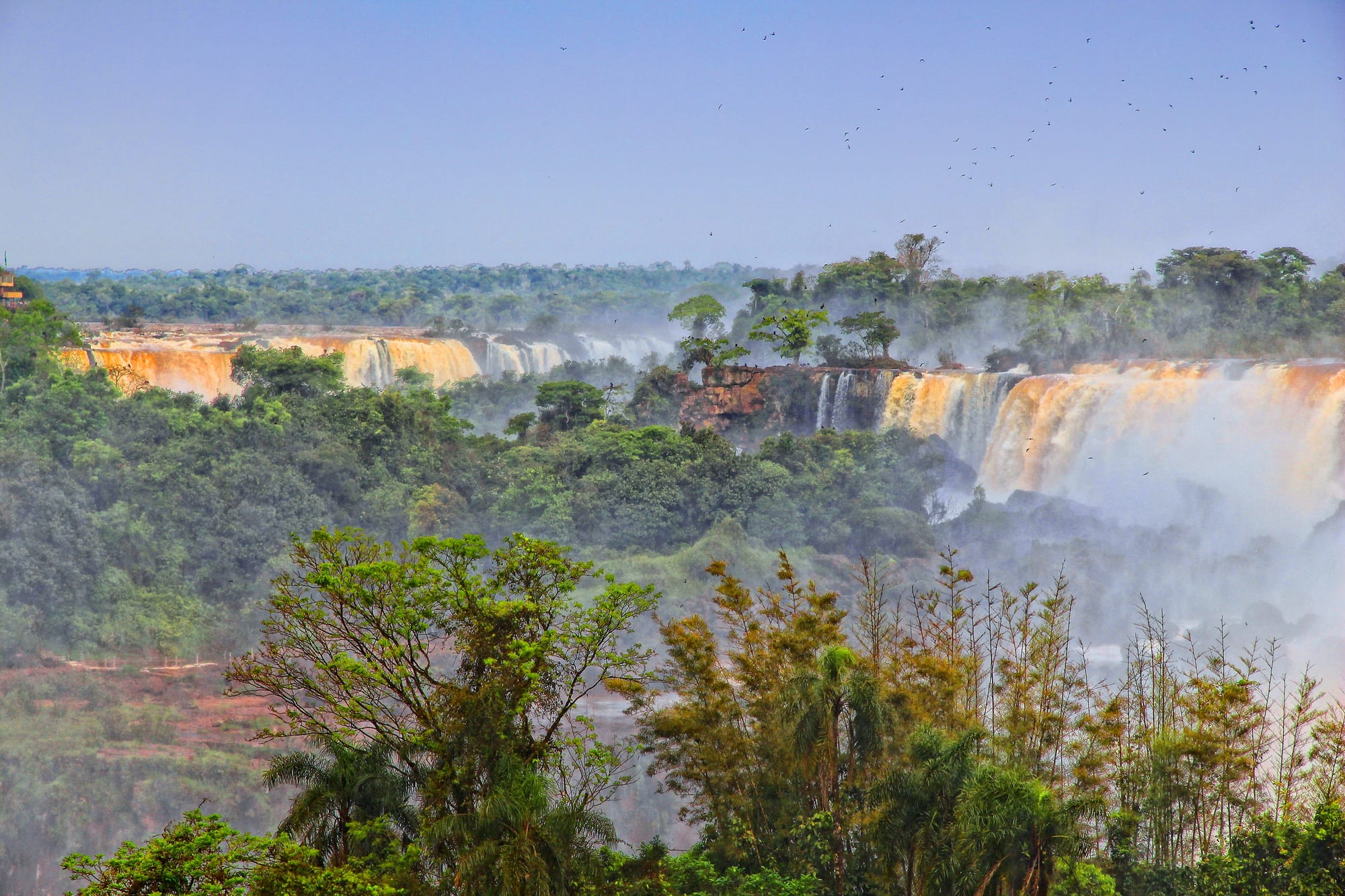 Several broad waterfalls pouring over cliffs into misty gorges, surrounded by dense green subtropical forest