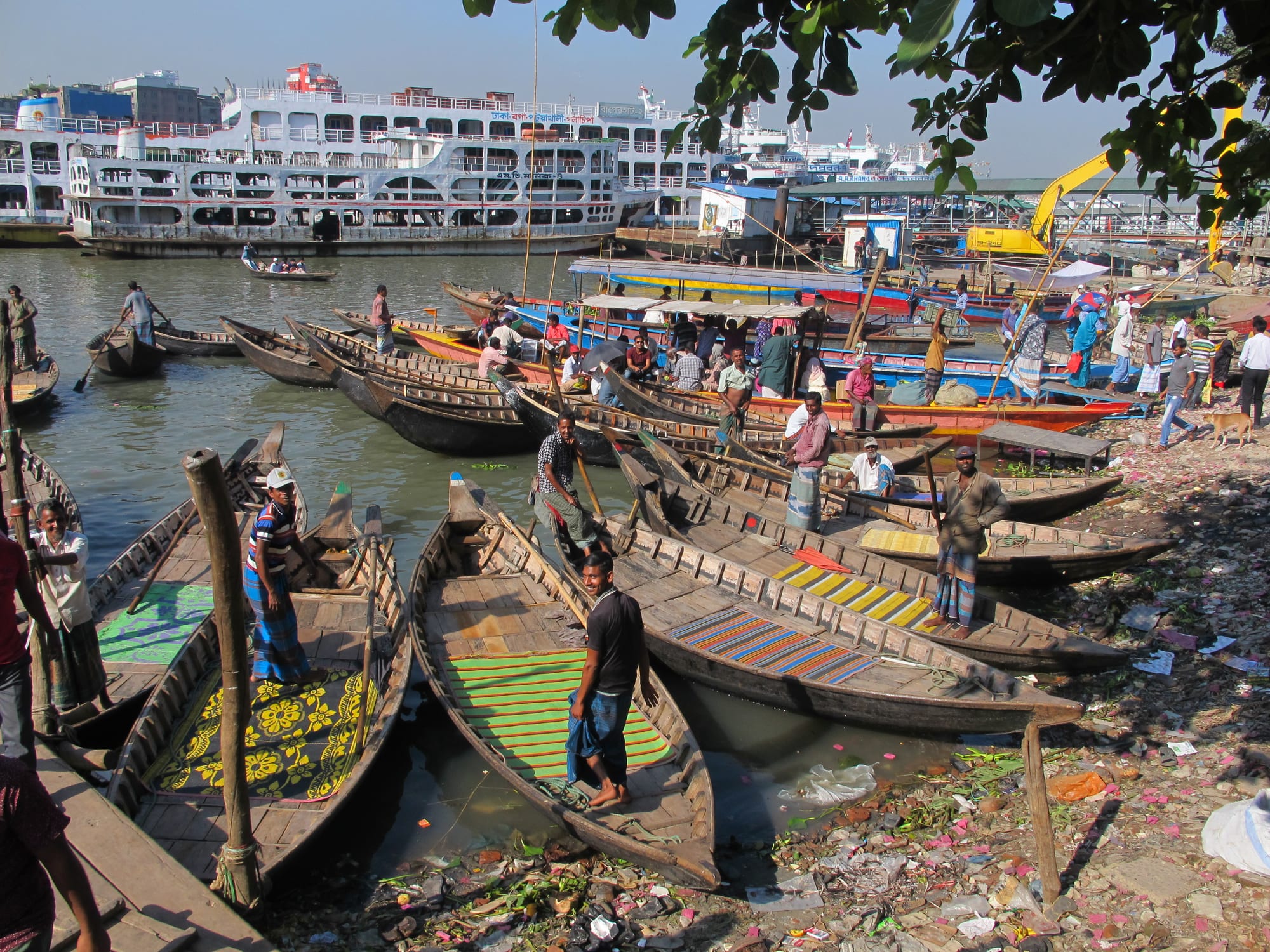Wooden rowing boats moored on the Buriganga shore, with large white passenger launches across the water