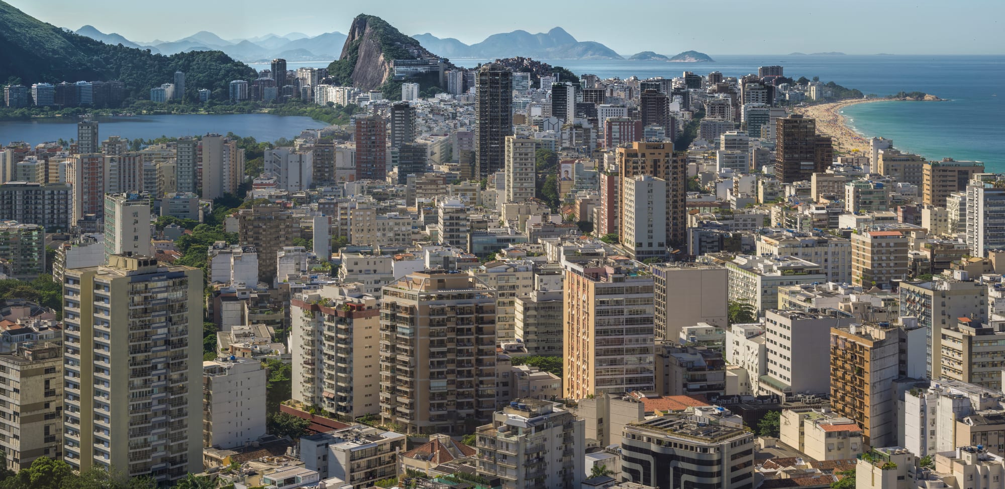 High-rise blocks of Leblon and Ipanema between a lagoon and the ocean, with granite peaks and a curving beach beyond