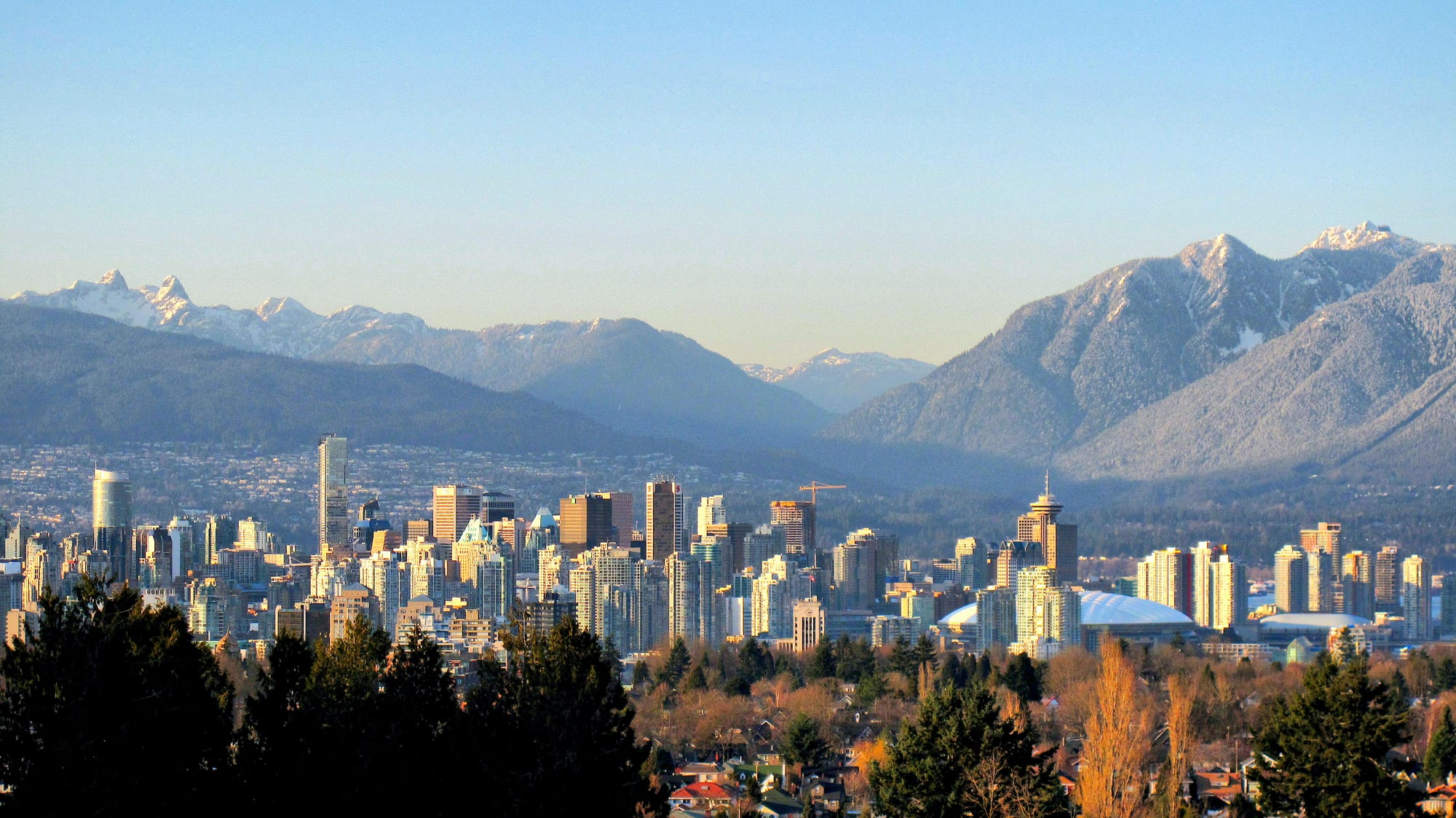 Downtown Vancouver's towers in low winter sun, with snow-dusted North Shore Mountains rising behind them