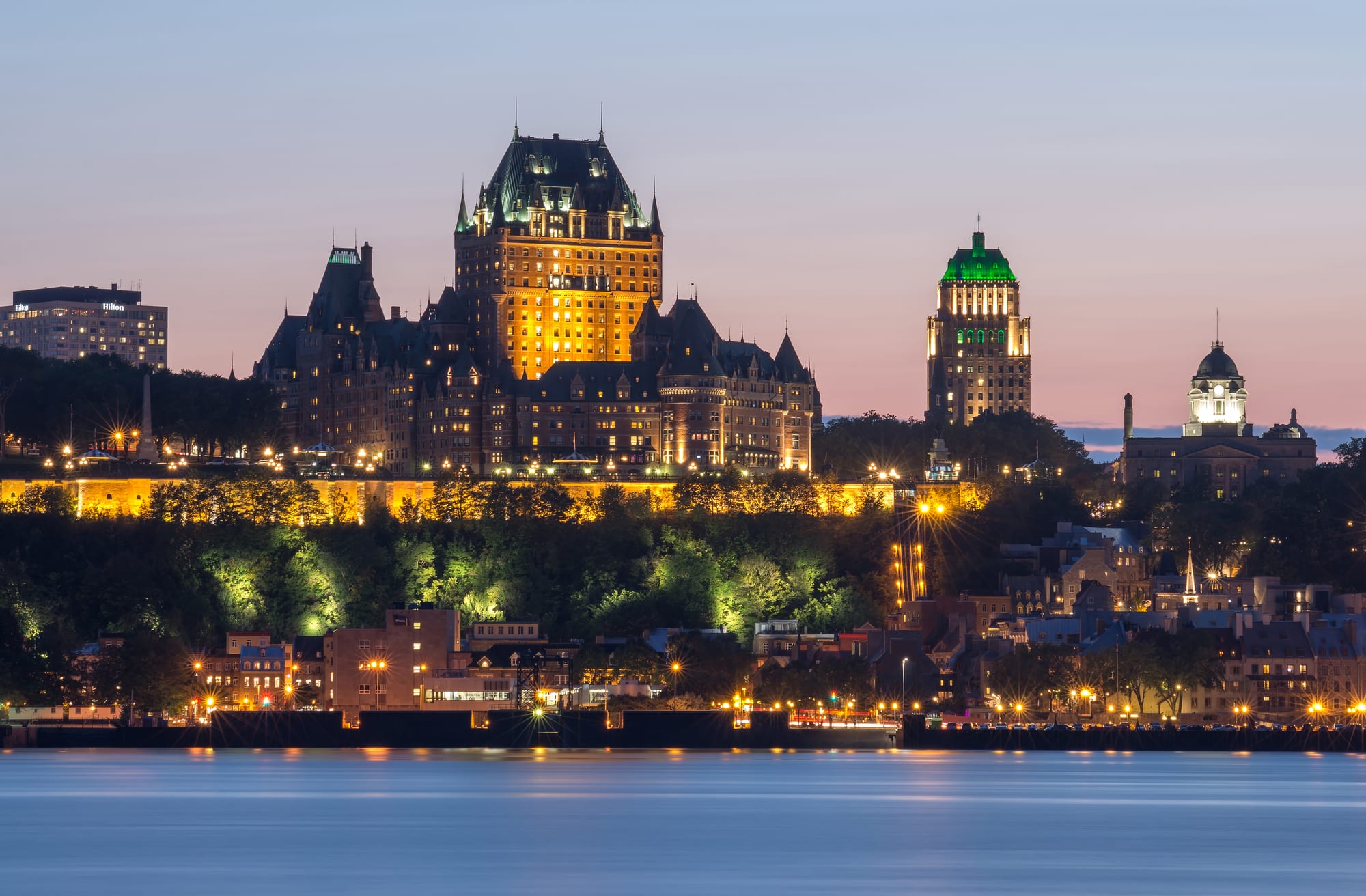The lit Château Frontenac and old town on a wooded cliff above the St Lawrence River at dusk
