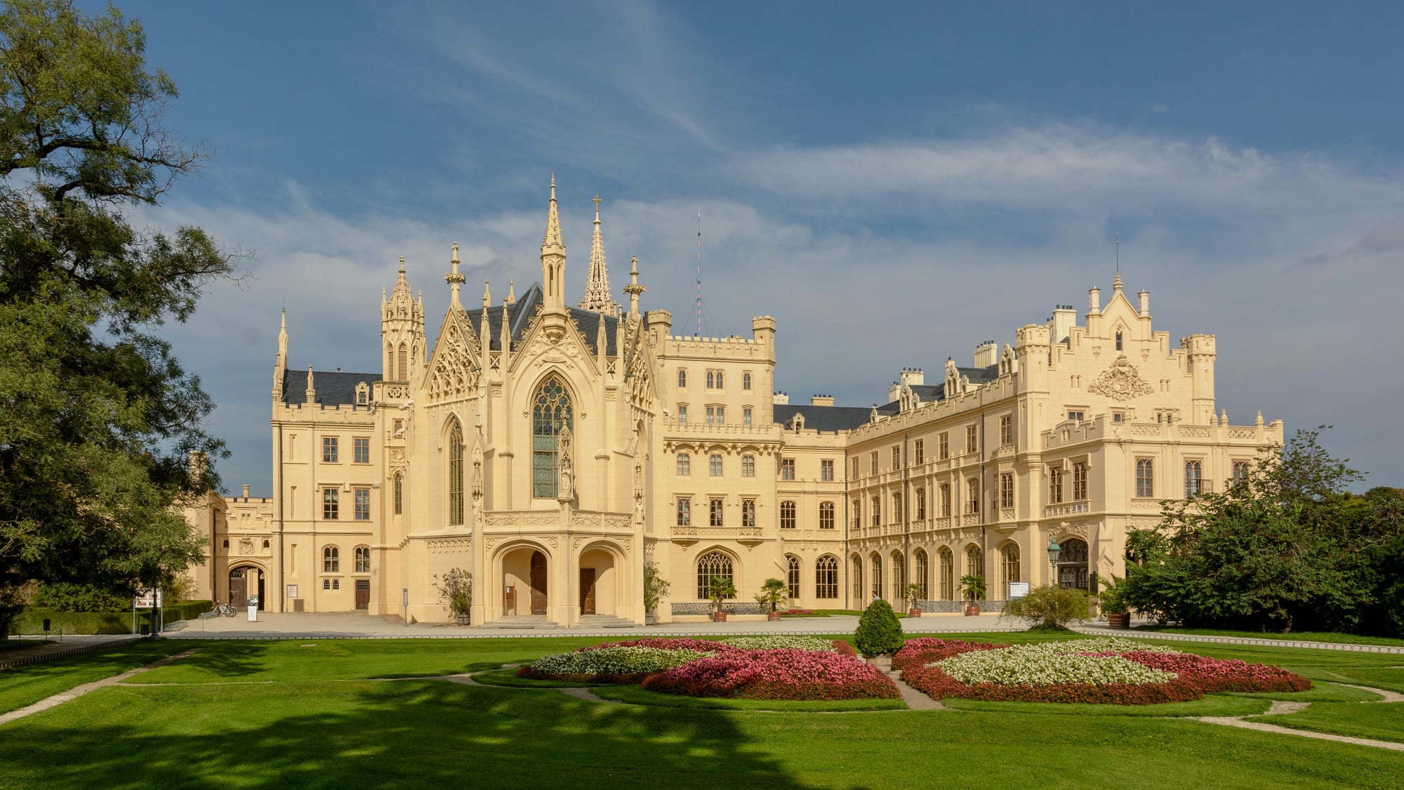 The pale neo-Gothic front of Lednice château with pointed spires and turrets, behind a lawn and flower beds