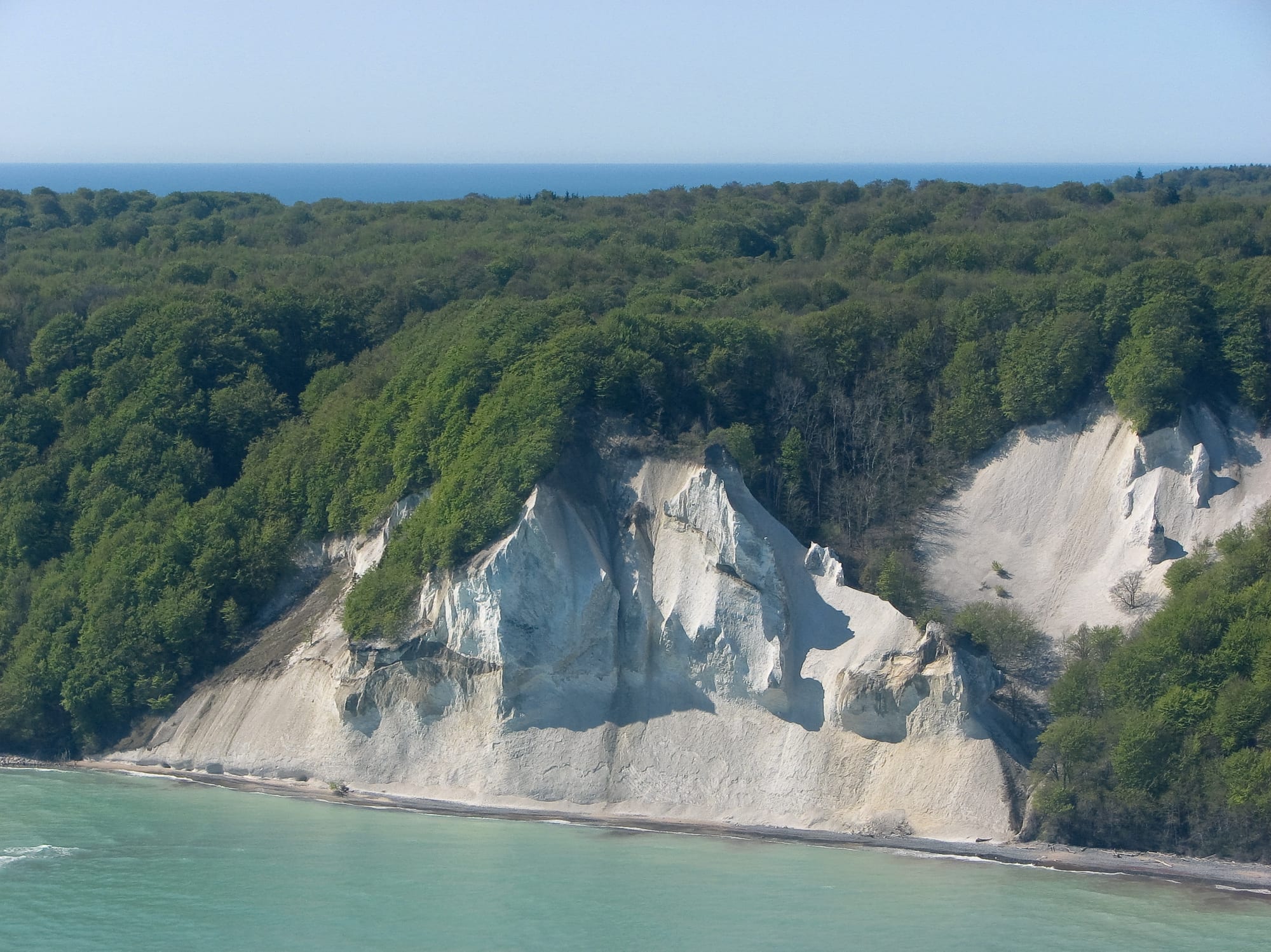 Aerial view of the white chalk cliffs of Møns Klint, topped with beech forest and dropping to a turquoise Baltic shore