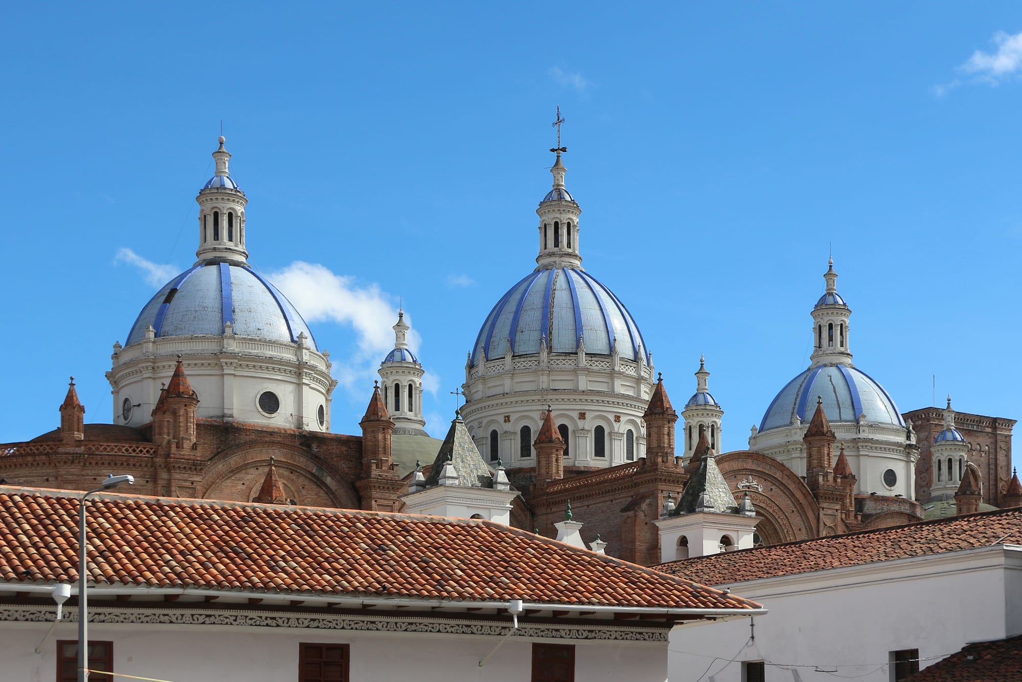Three large blue-and-white tiled domes on a brick cathedral rising above red tile roofs under a blue sky