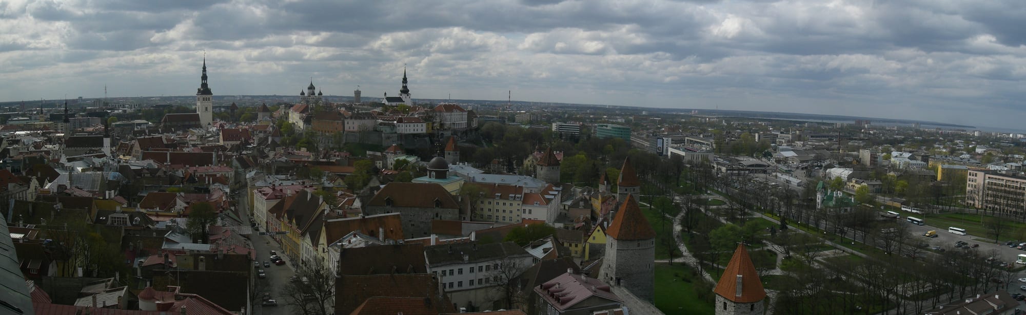 A dense cluster of medieval red-tiled roofs, church spires, and stone towers seen from above under a bright sky