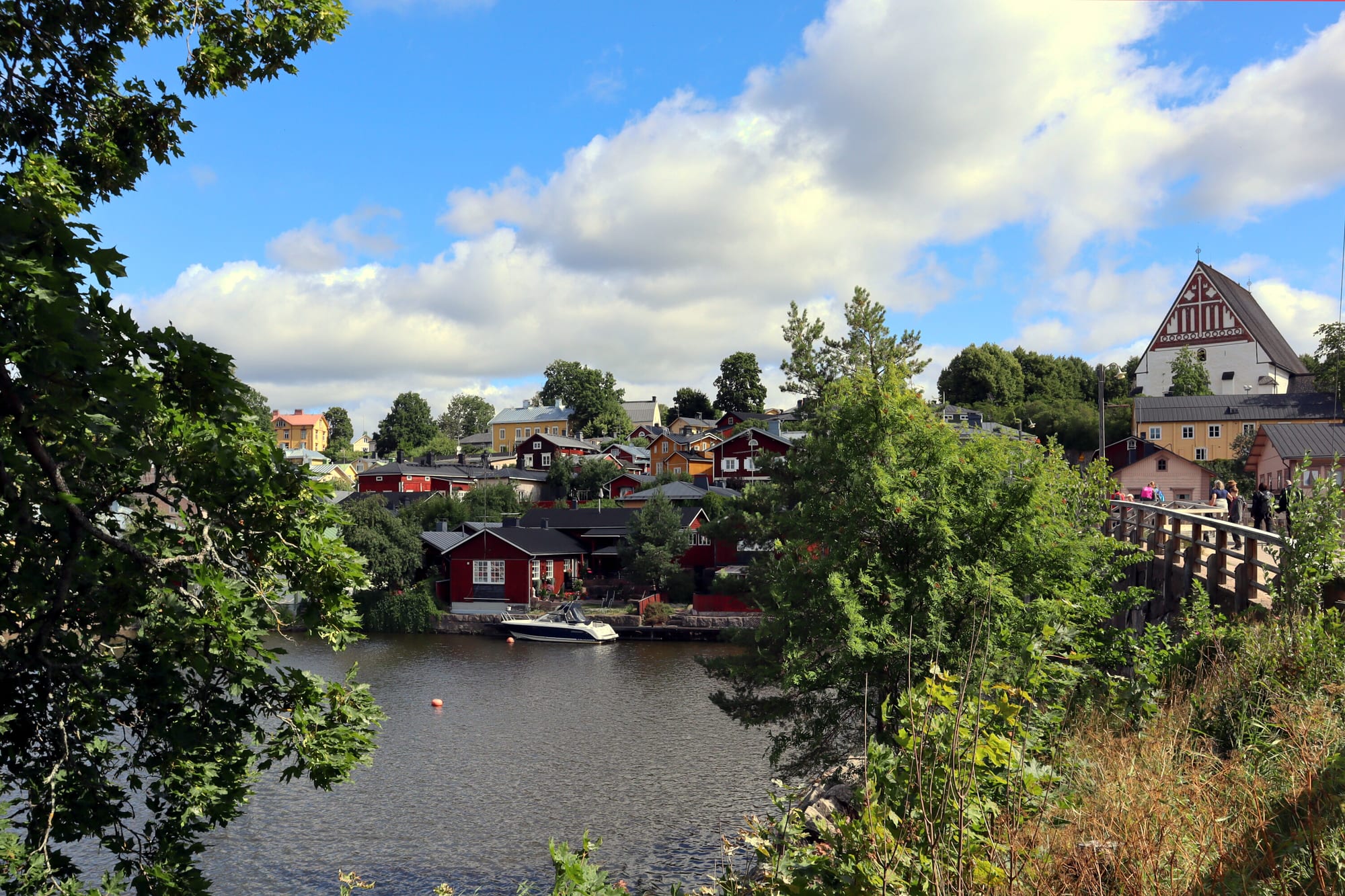 Red and ochre wooden houses of Porvoo's old town along a river in summer, with the white-gabled cathedral on the hill above