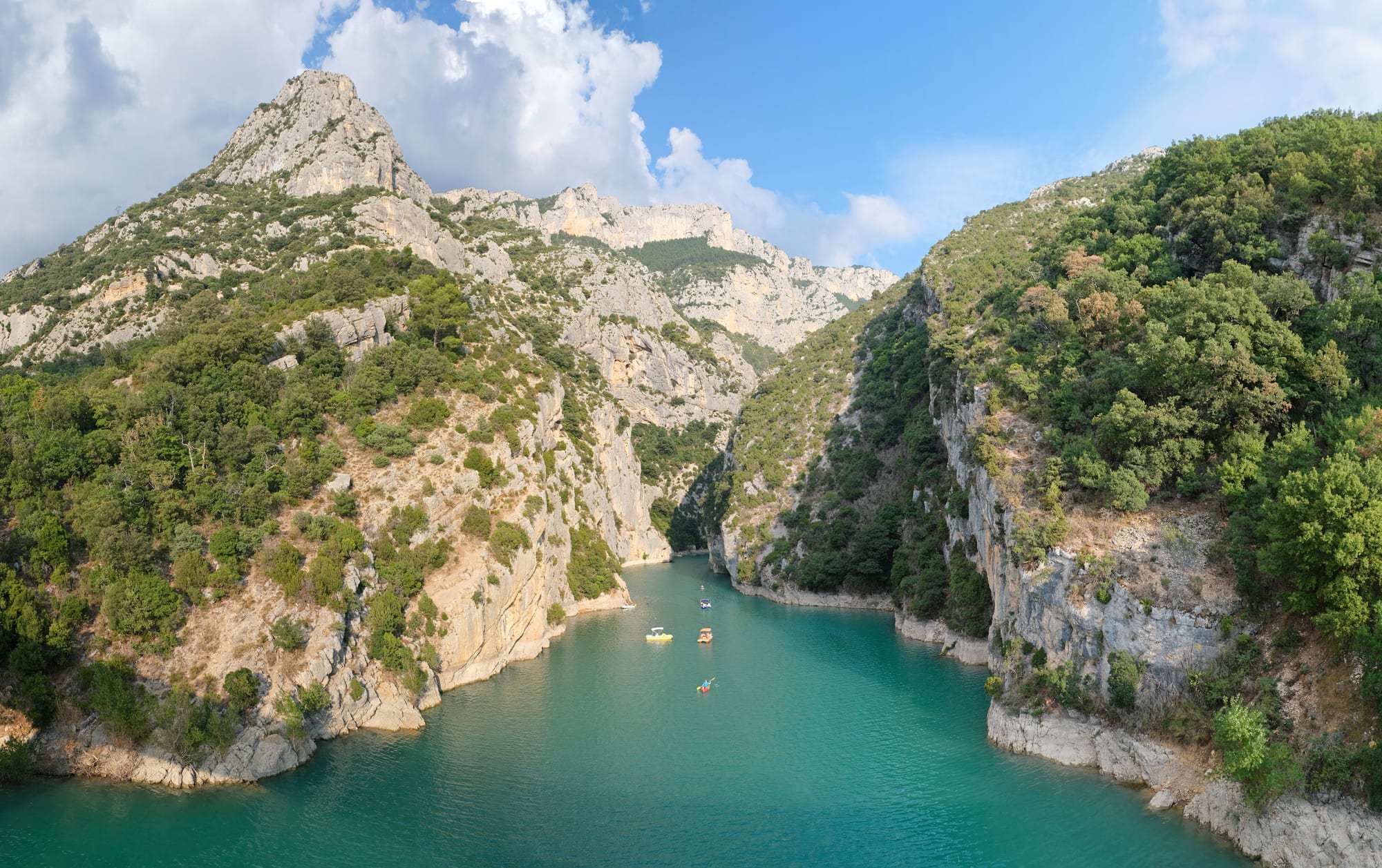 Turquoise river water between steep limestone cliffs and wooded slopes, with small pedal boats on the water
