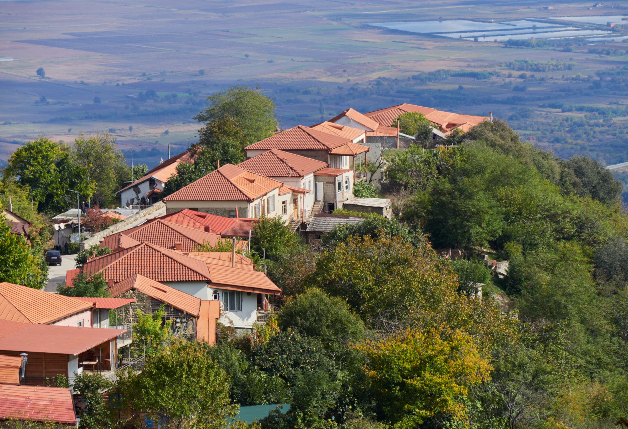 Red-roofed houses of a hilltop town among autumn trees, with the flat farmland of a wide valley far below