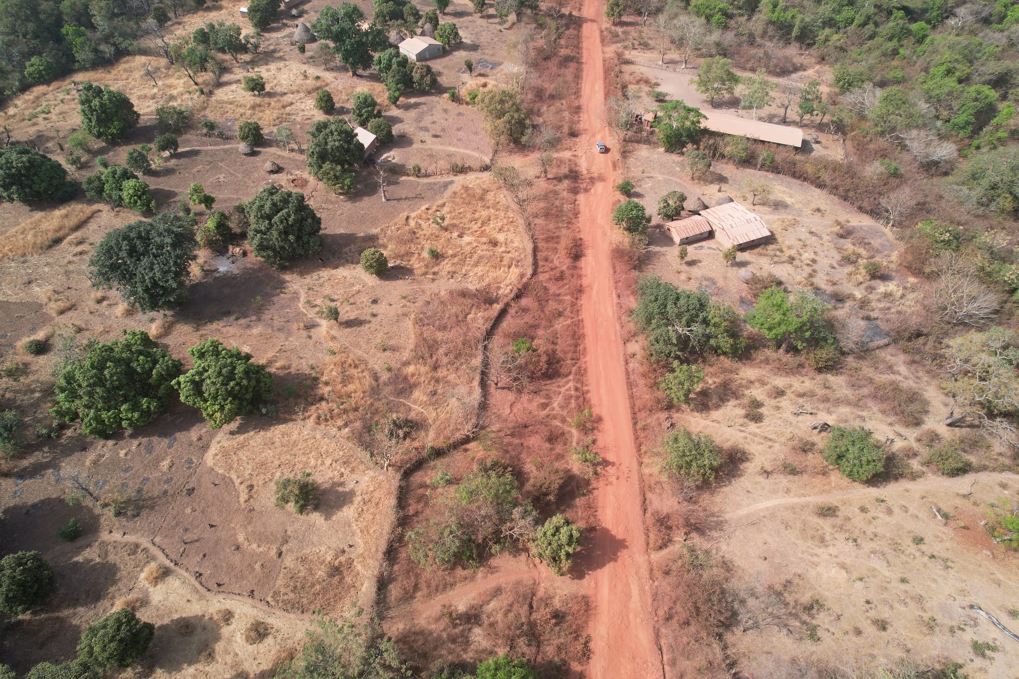 Aerial view of a red dirt road running past scattered houses, trees and dry fields in the dry season