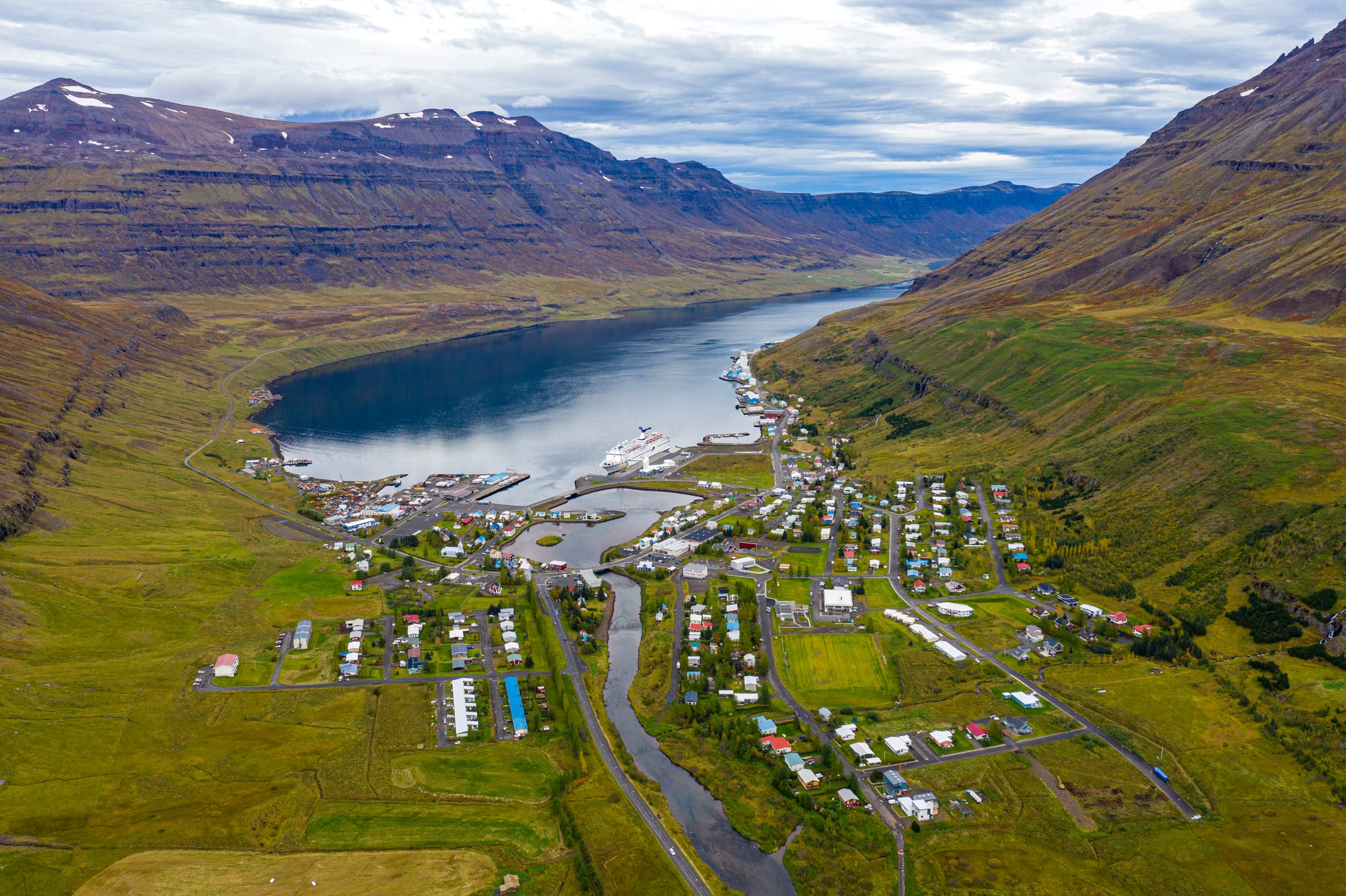Aerial view of Seyðisfjörður town at the head of a narrow fjord between steep terraced mountains, a ship at the quay