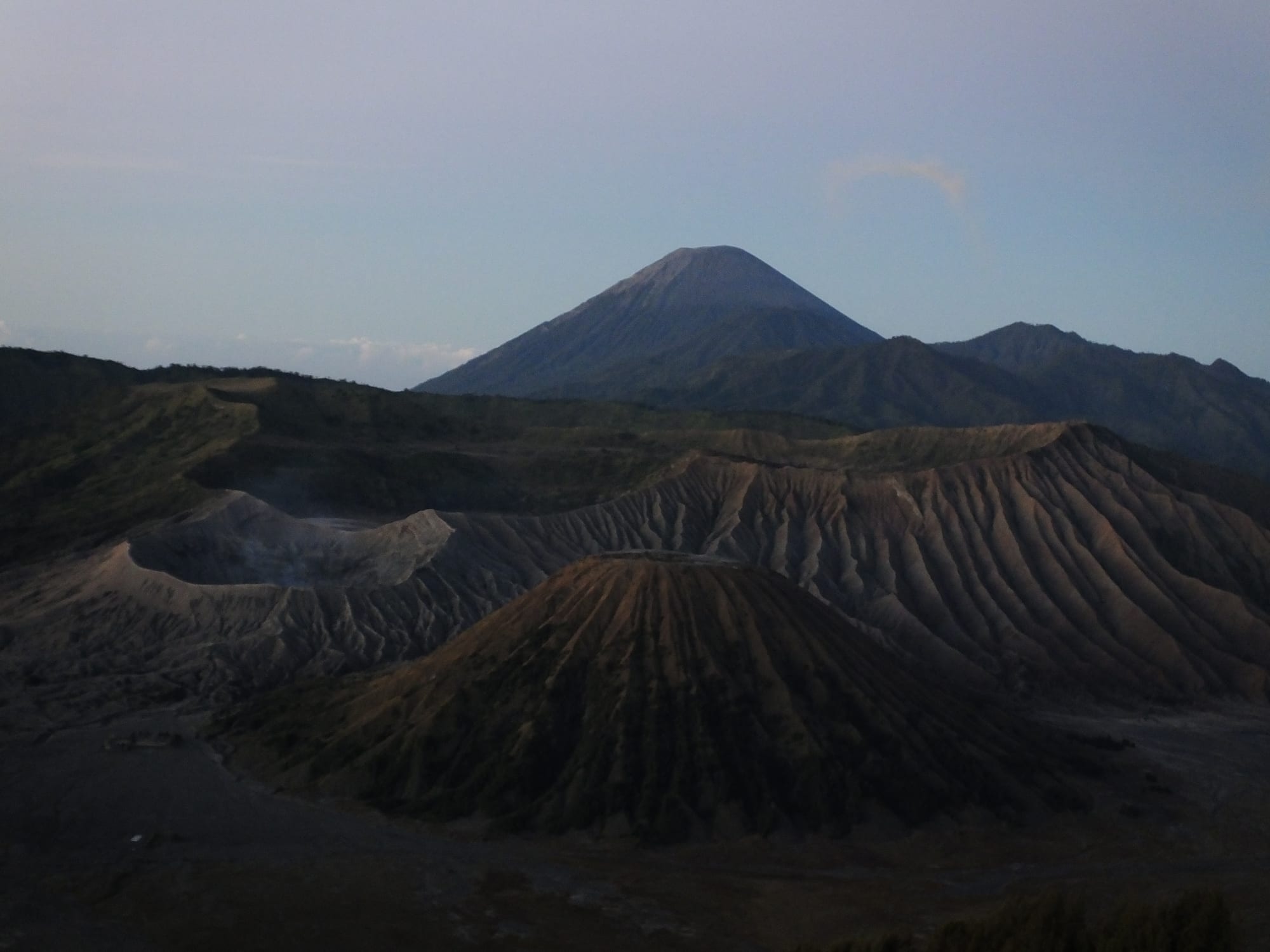 Grey ash cones of Mount Batok and the Bromo crater at dawn, with the peak of Semeru rising behind