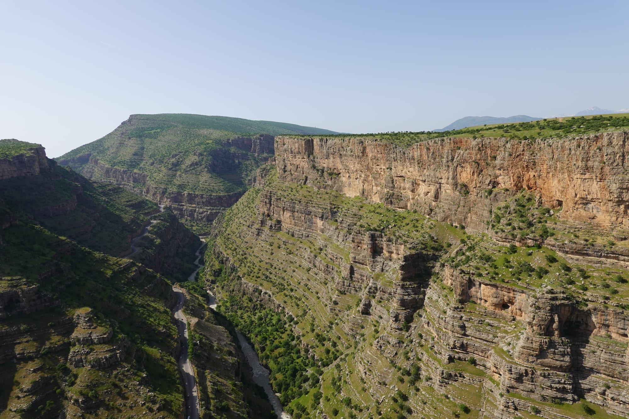 A deep green canyon with sheer orange limestone cliffs, a road and river winding along the valley floor