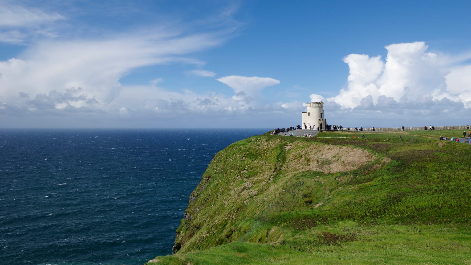 Sheer dark sea cliffs dropping hundreds of feet to the Atlantic, grassy clifftop in the foreground under a bright sky