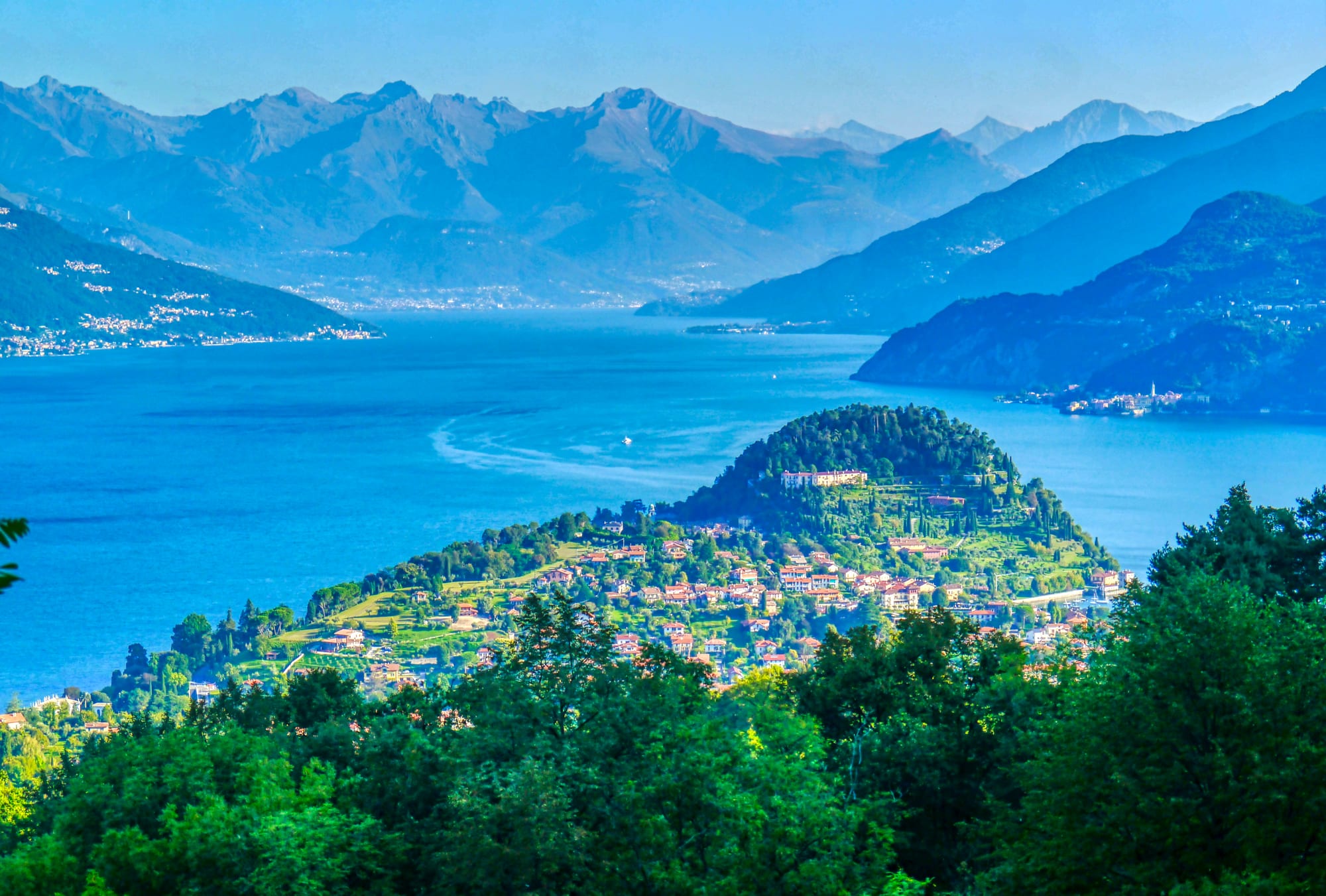 The wooded promontory and village of Bellagio jutting into a blue lake, with layered mountains behind