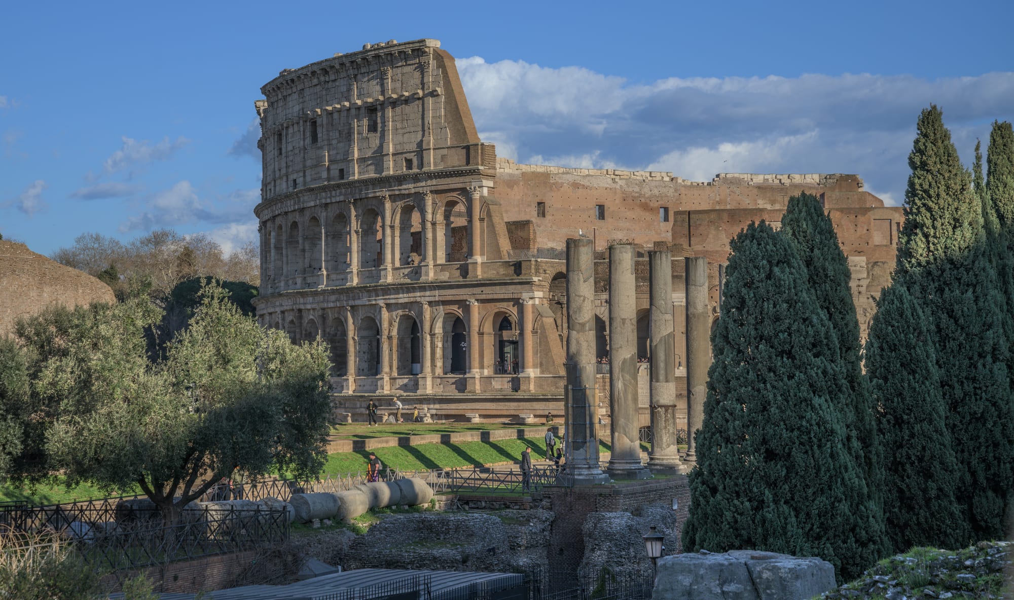 The great oval stone amphitheatre of the Colosseum, its tiered arches partly ruined, with the Roman Forum beside it