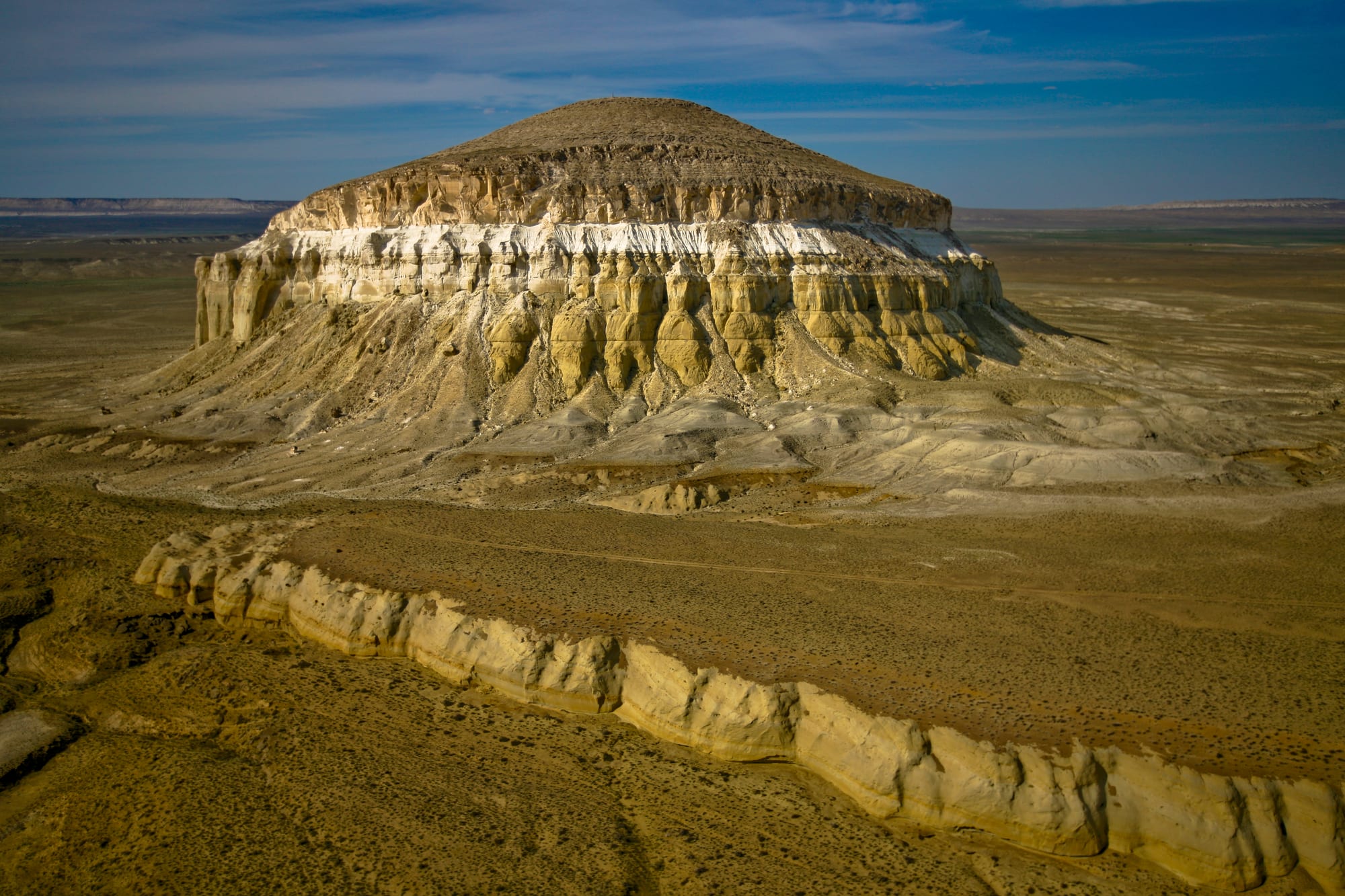A lone flat-topped hill with pale, eroded chalk cliffs rising from a flat brown desert plain