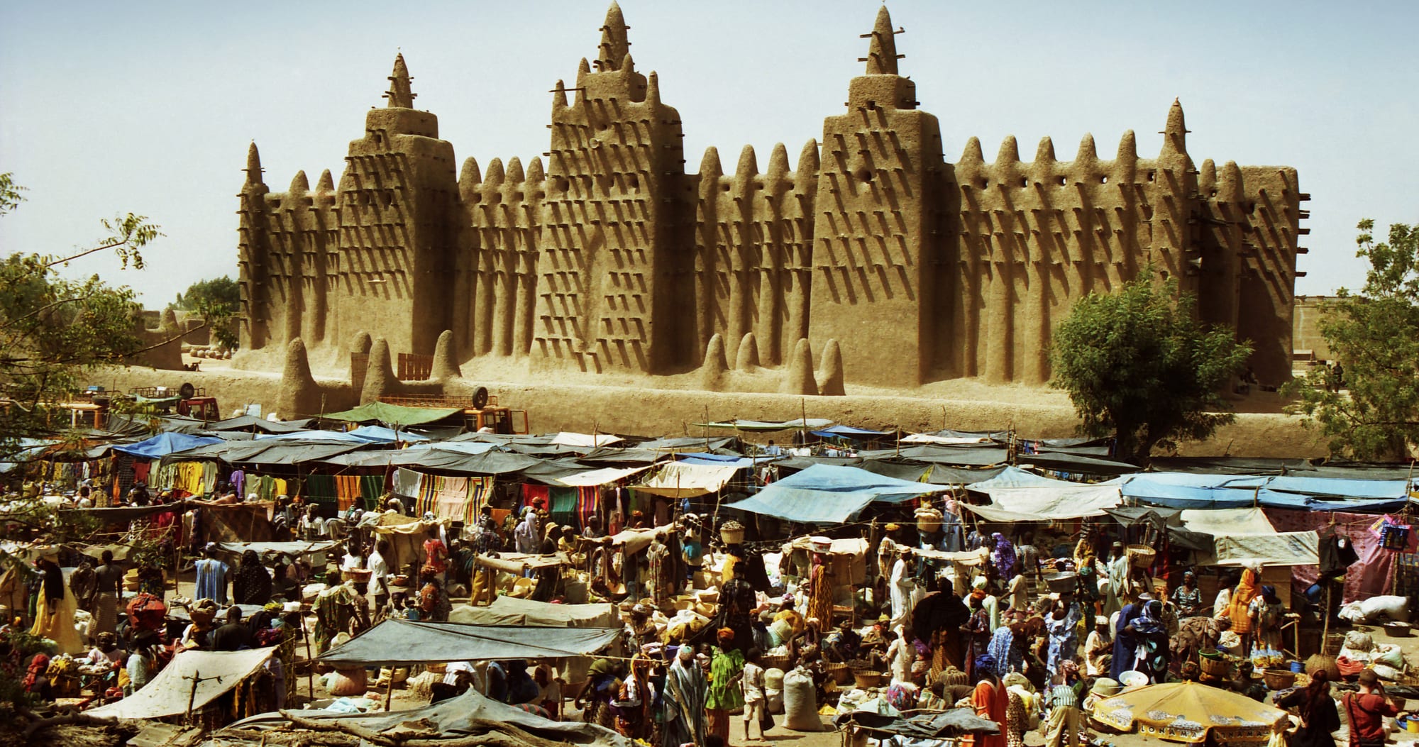 A vast mosque built entirely of sun-dried mud, bristling with wooden beams and topped by three tapering towers, above a market square