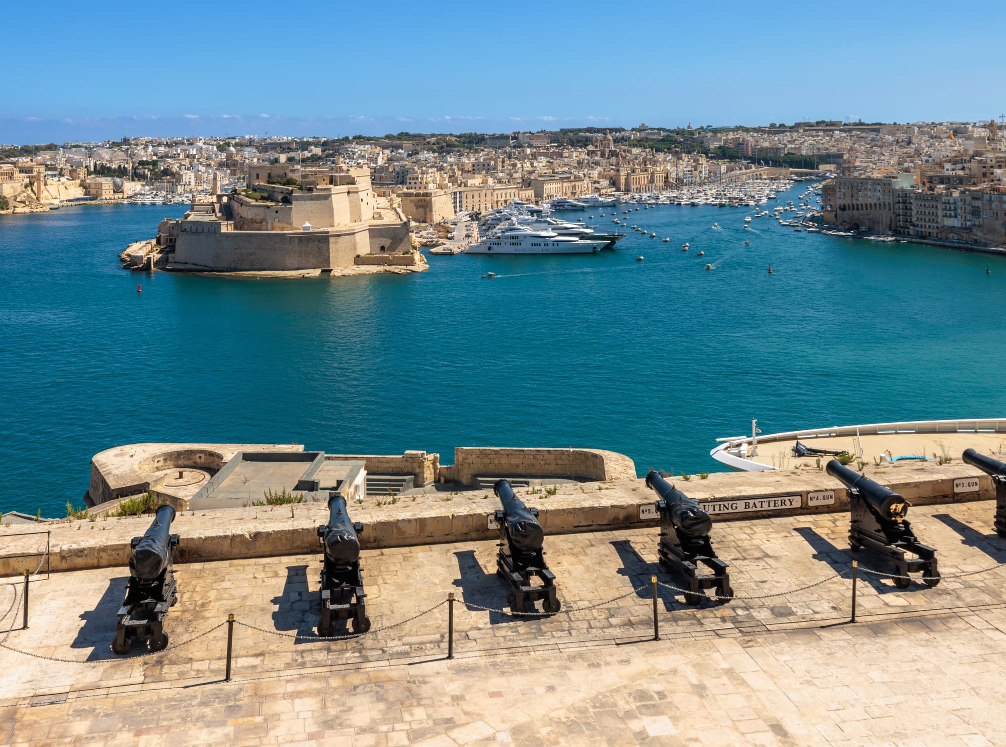 The fortified honey-coloured skyline of Valletta with church domes and bastions, seen across the blue water of the Grand Harbour