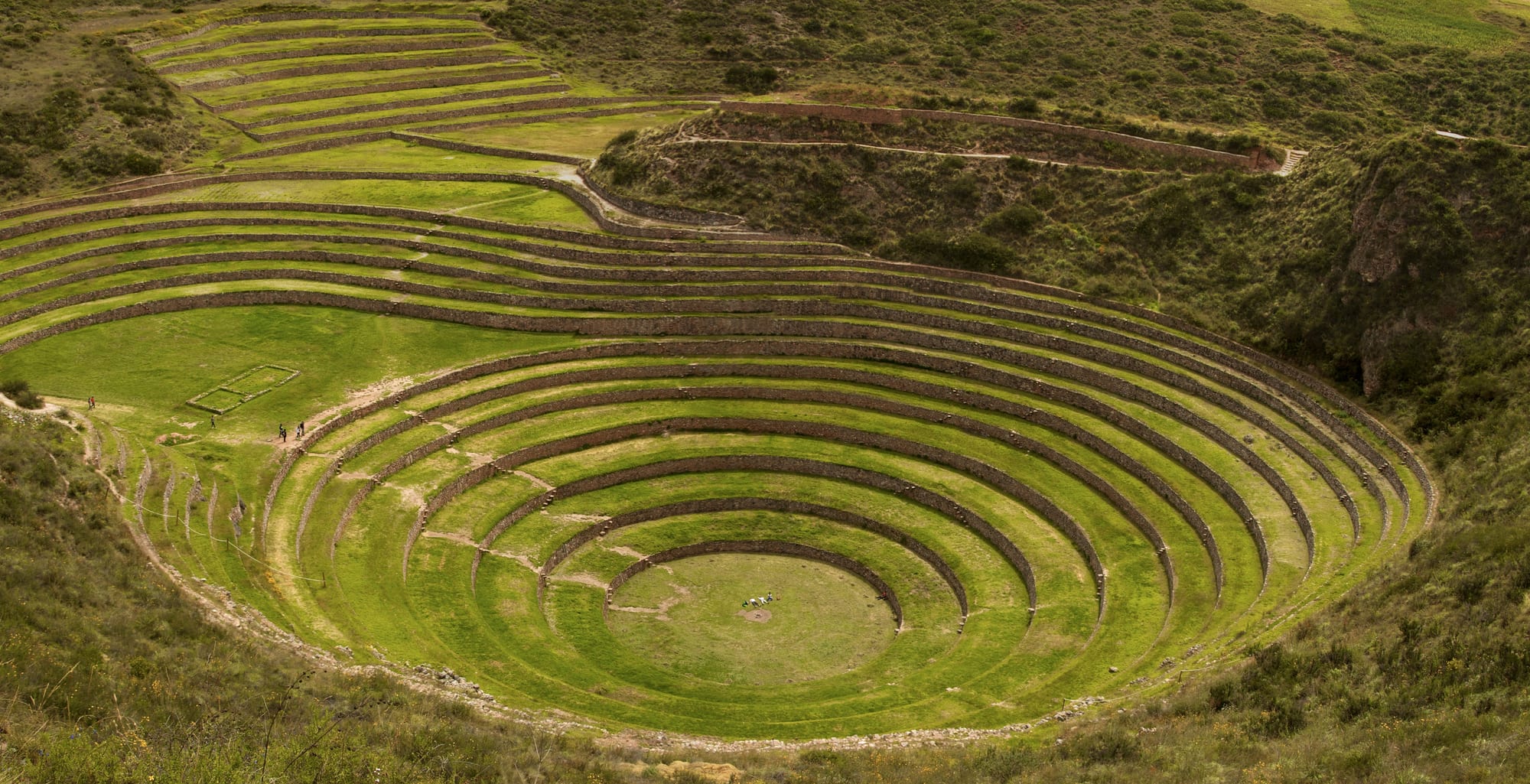 Grassy circular stone terraces descending in rings into a deep round hollow in green hills