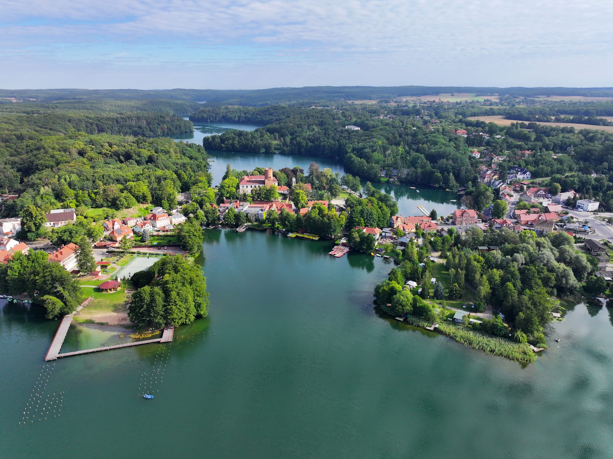 Aerial view of a village with a red-brick castle tower between two green lakes surrounded by forest