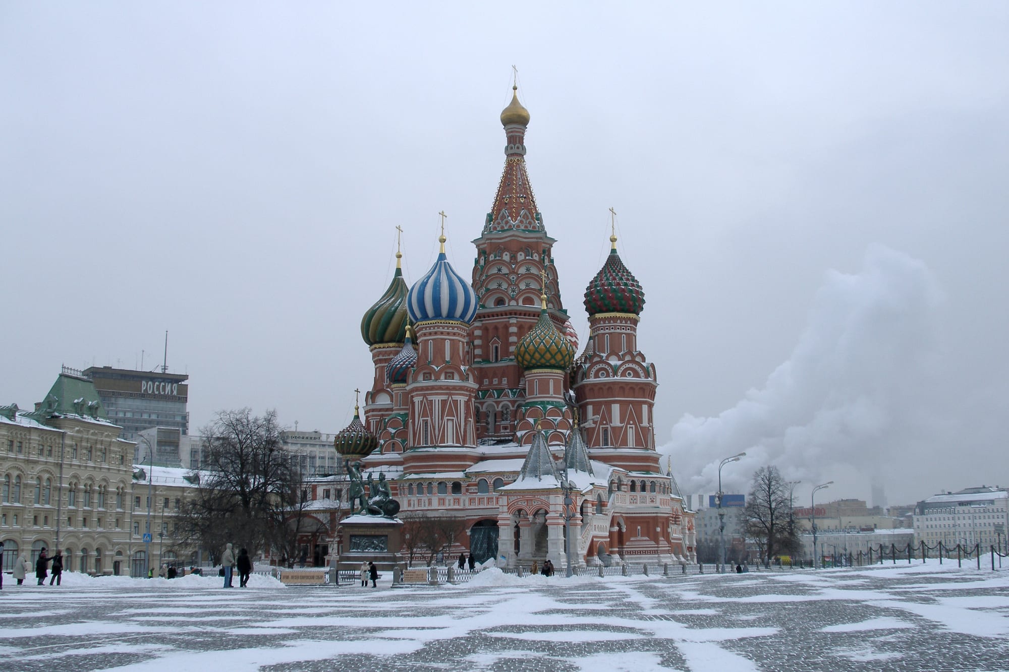 A cluster of brightly coloured, patterned onion domes on a stone Orthodox cathedral, seen across the open expanse of Red Square under a clear sky