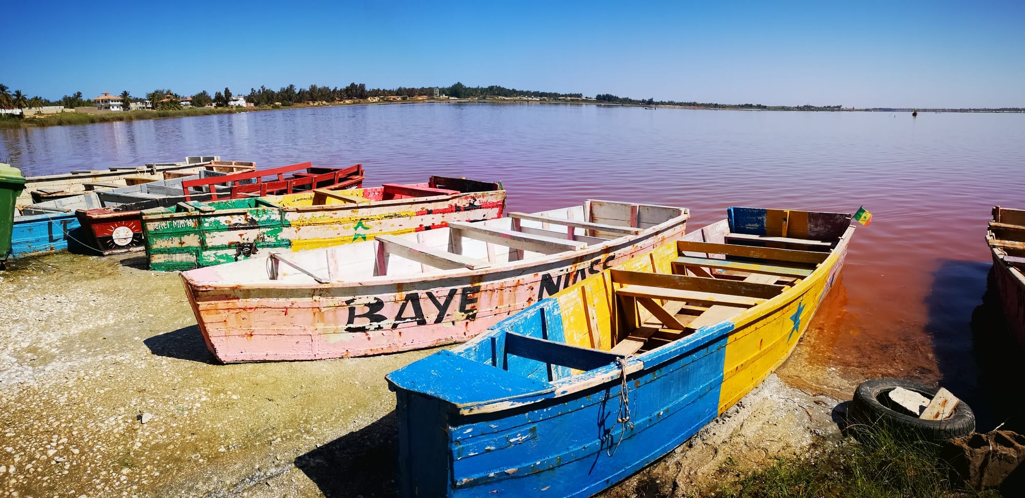 Painted wooden boats pulled up on the shore of a pink-tinged lake under a clear blue sky