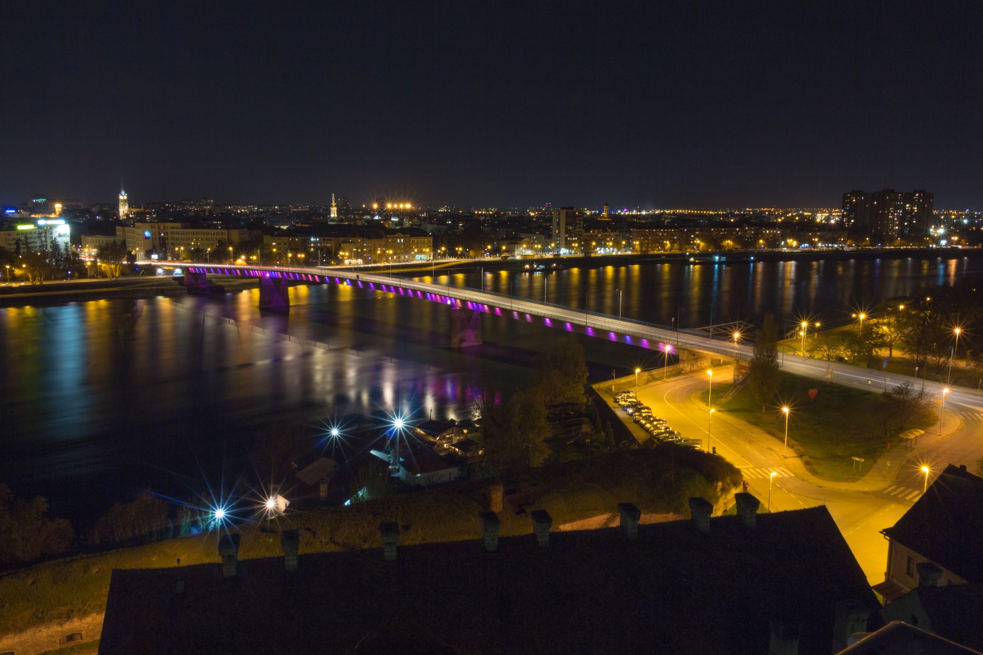 A star-shaped stone fortress on a bluff above a broad river, with a bridge crossing to a low riverside city and green hills beyond