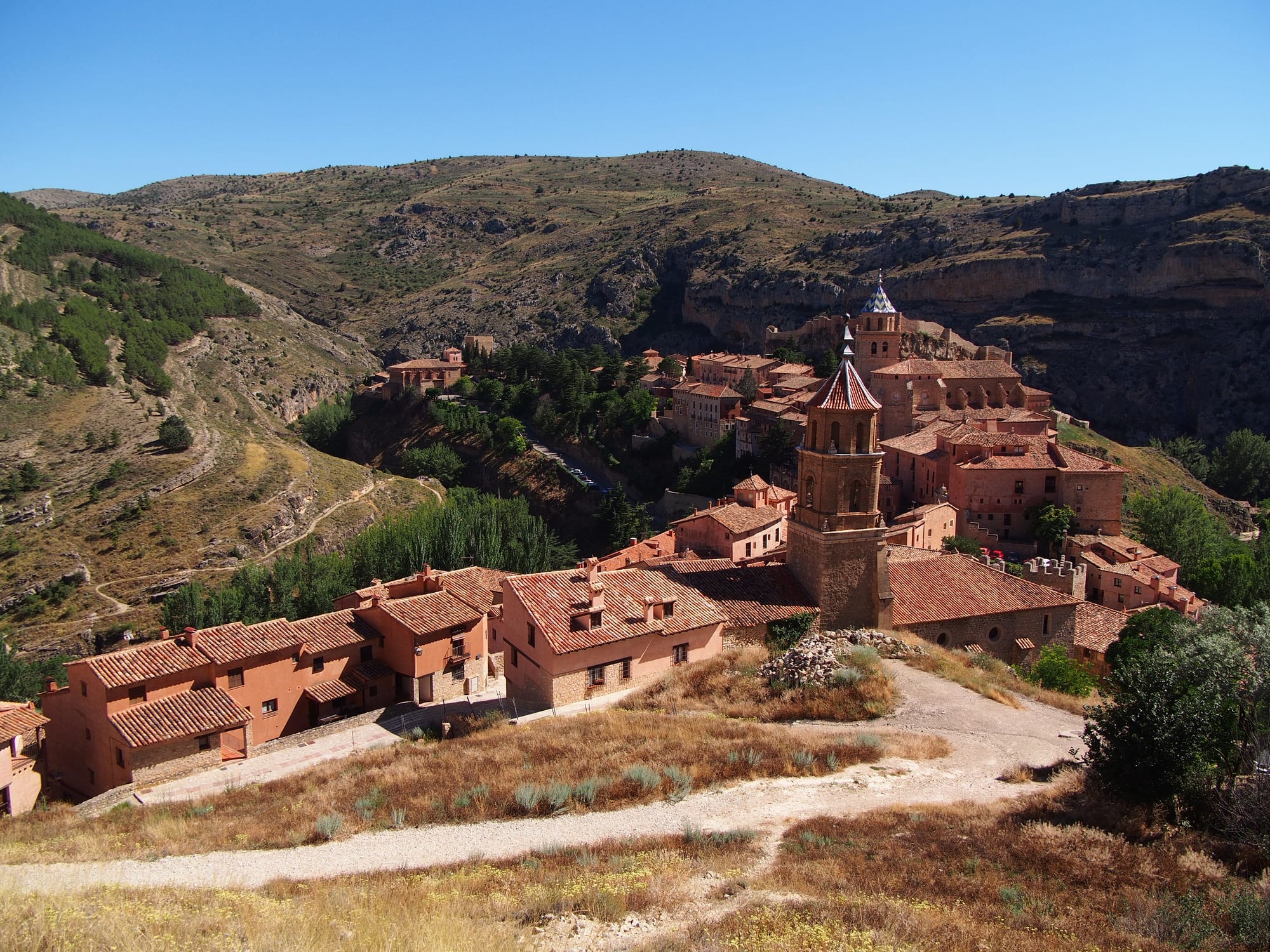 Pinkish stone houses and a church tower of Albarracín spread across a hillside above a rocky river gorge