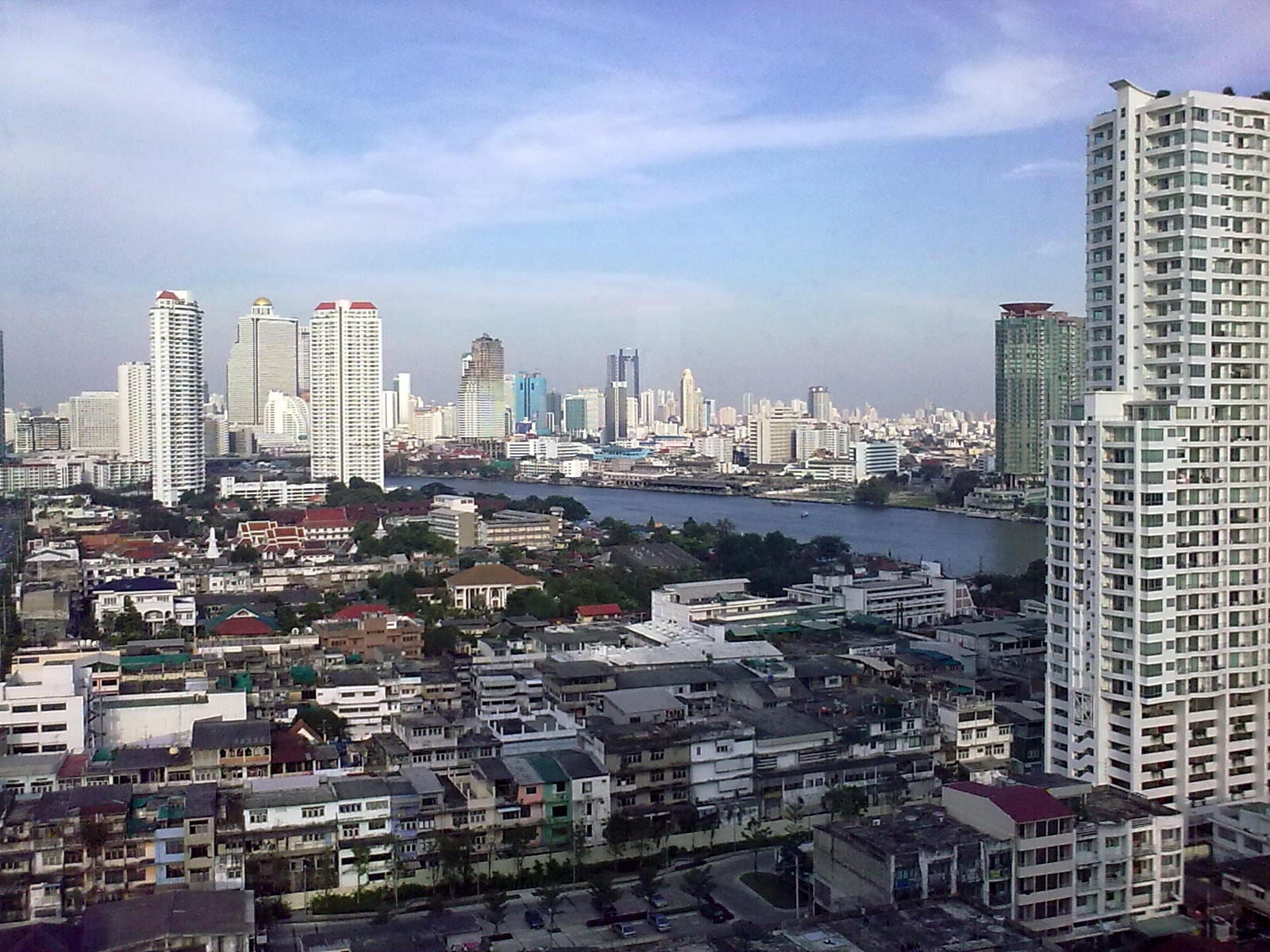 High-rise towers of Bangkok along a wide bend of the Chao Phraya River, with low-rise houses in the foreground