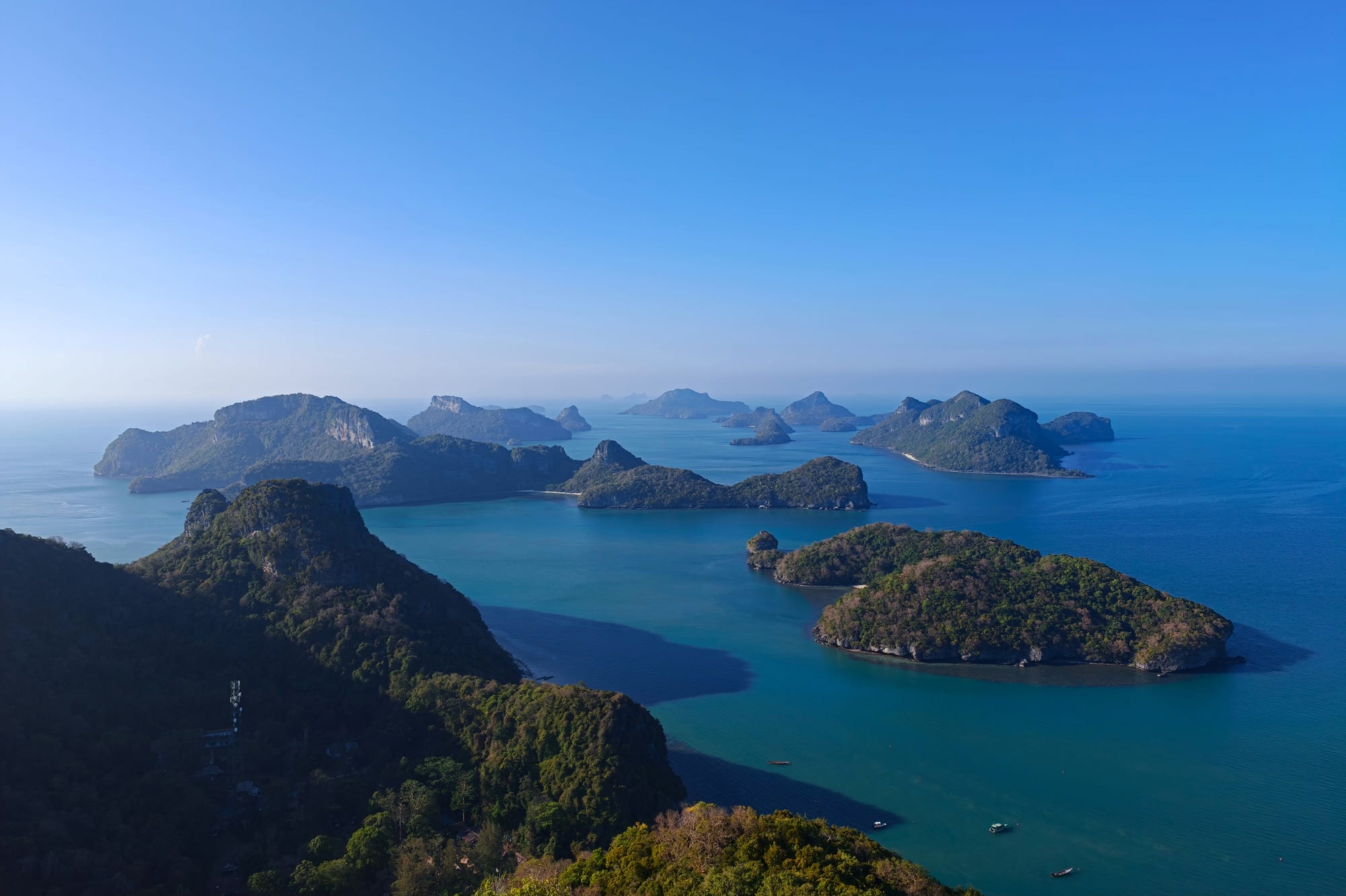 Forested limestone islands scattered across a calm blue sea, seen from a green hilltop under a clear sky