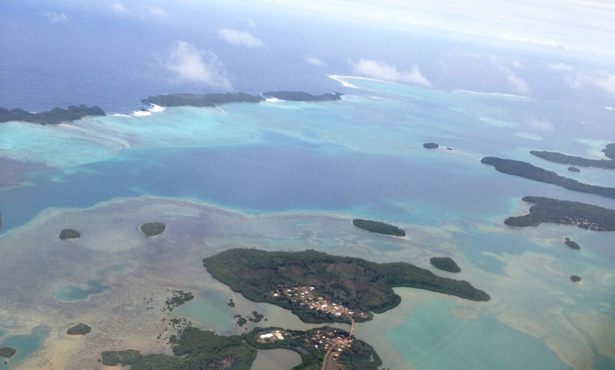 Aerial view of forested islands and reefs scattered across a calm blue sea under a partly clouded sky