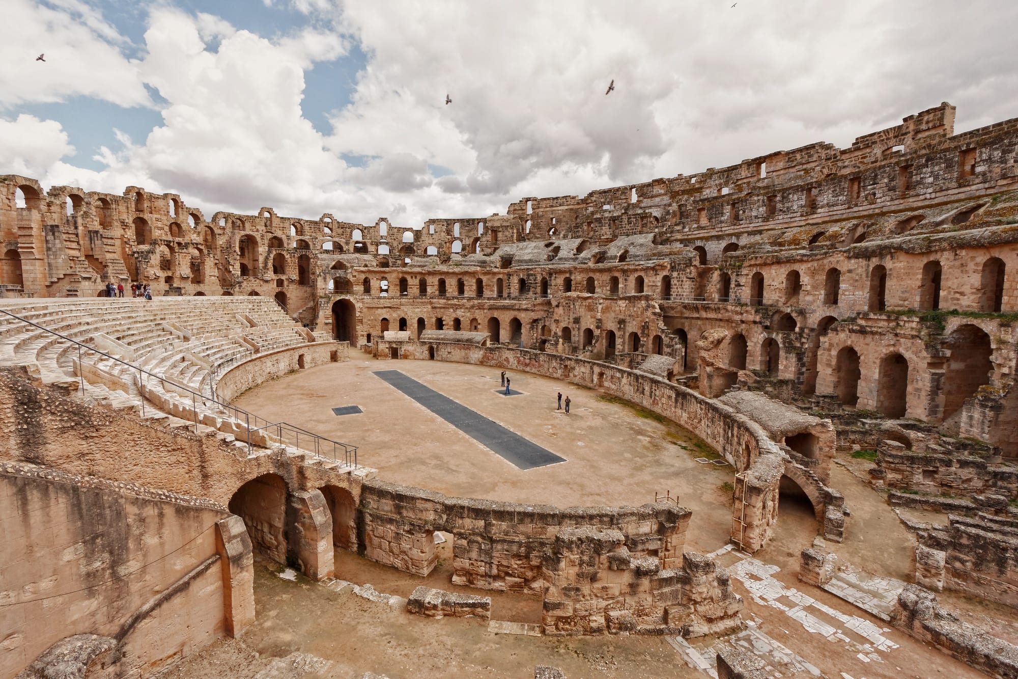 A huge, well-preserved Roman amphitheatre of golden stone standing amid a low modern town under a clear sky