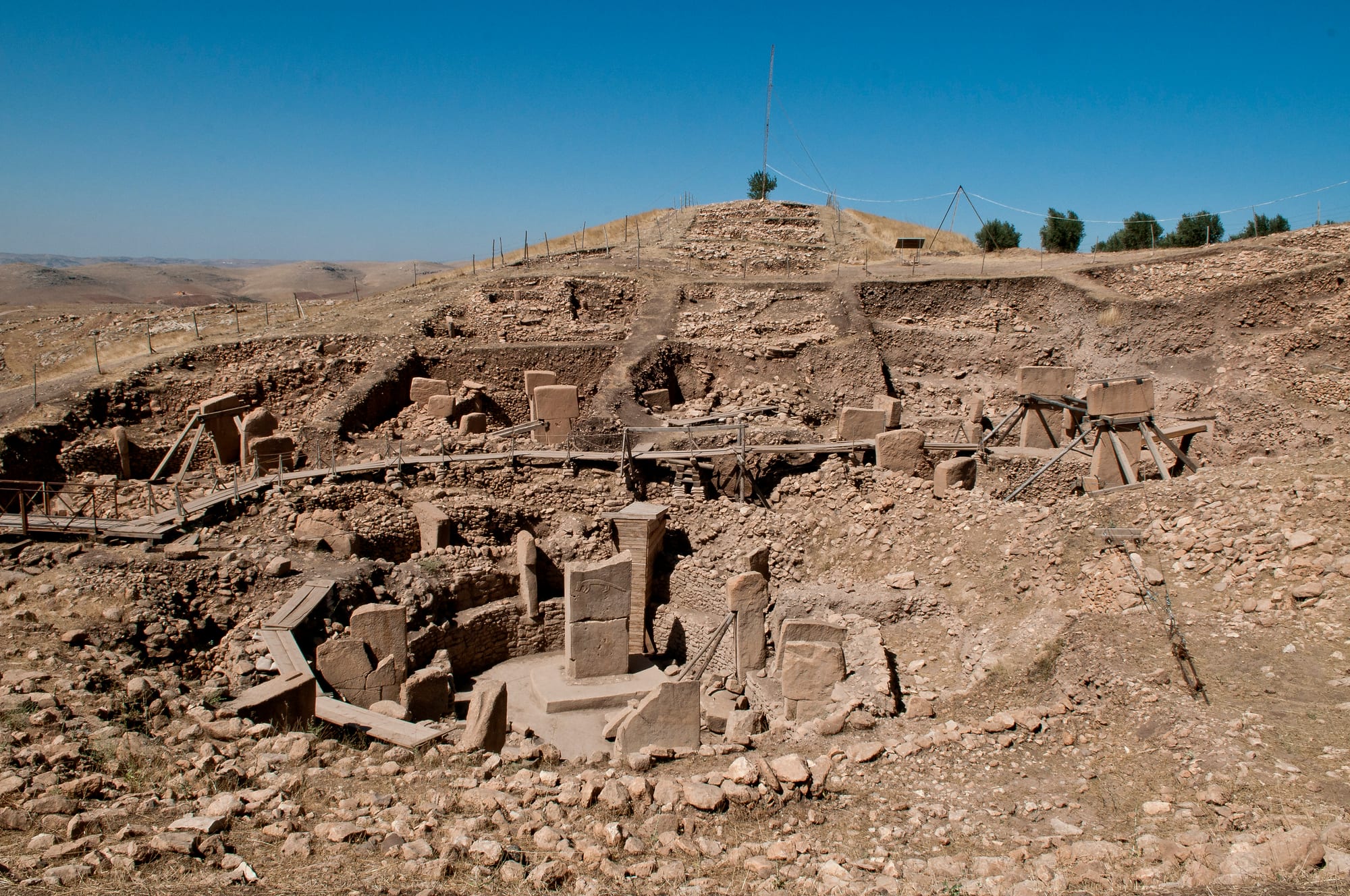 Excavated circular enclosures of stone walls and T-shaped pillars on a dry hilltop under a clear blue sky