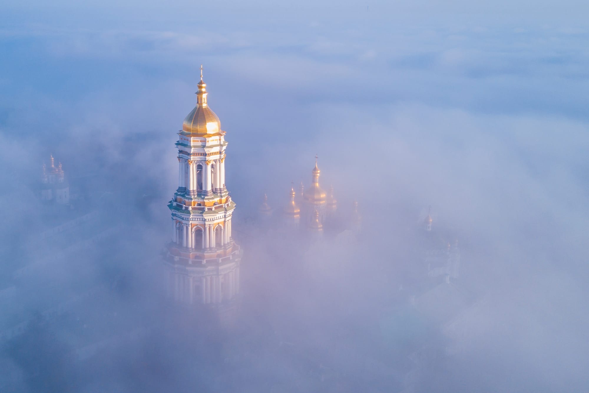 The gilded bell tower and golden domes of the Kyiv Pechersk Lavra rising above a thick morning mist