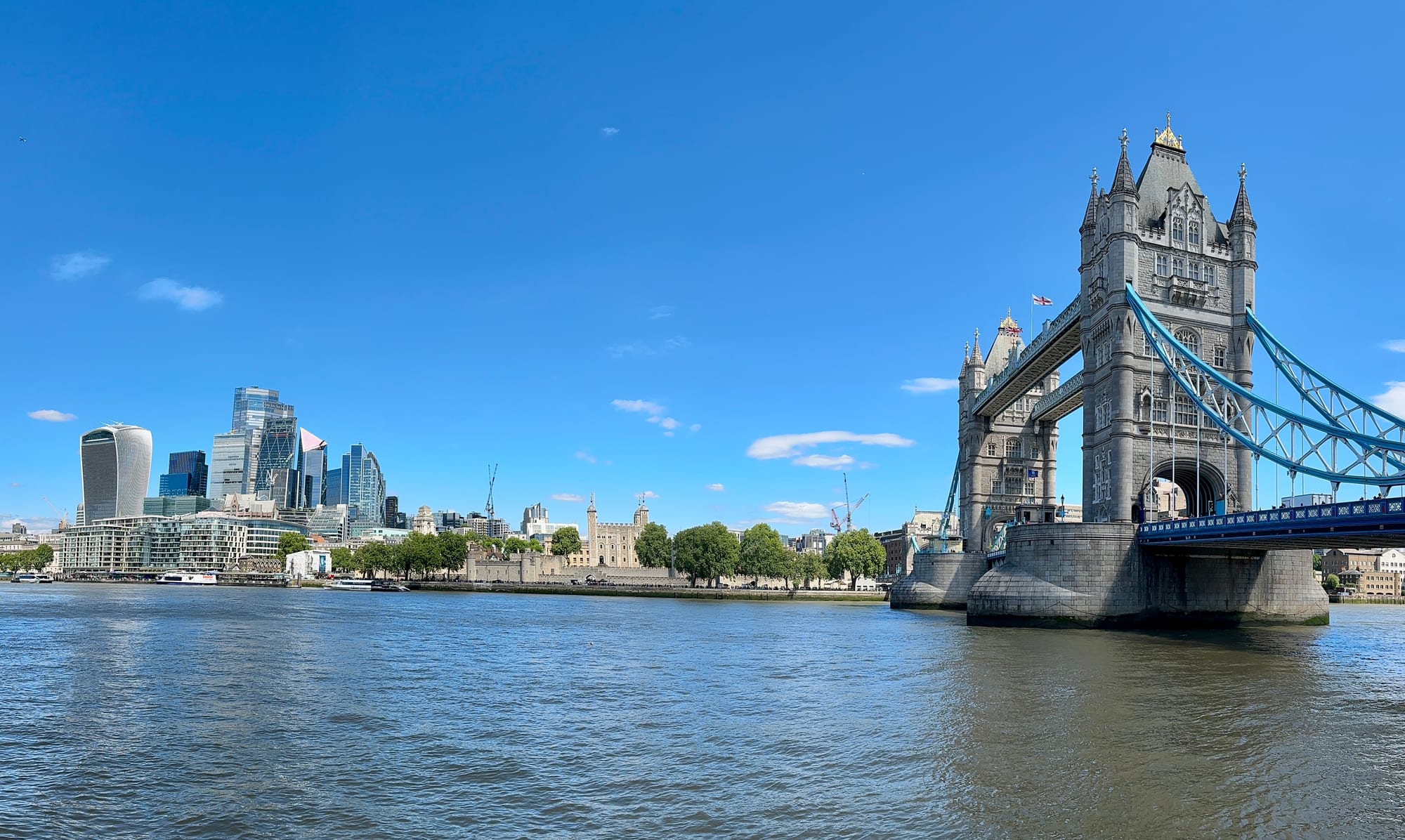 Tower Bridge on the right across the Thames, with the Tower of London and the City's glass towers under a blue sky