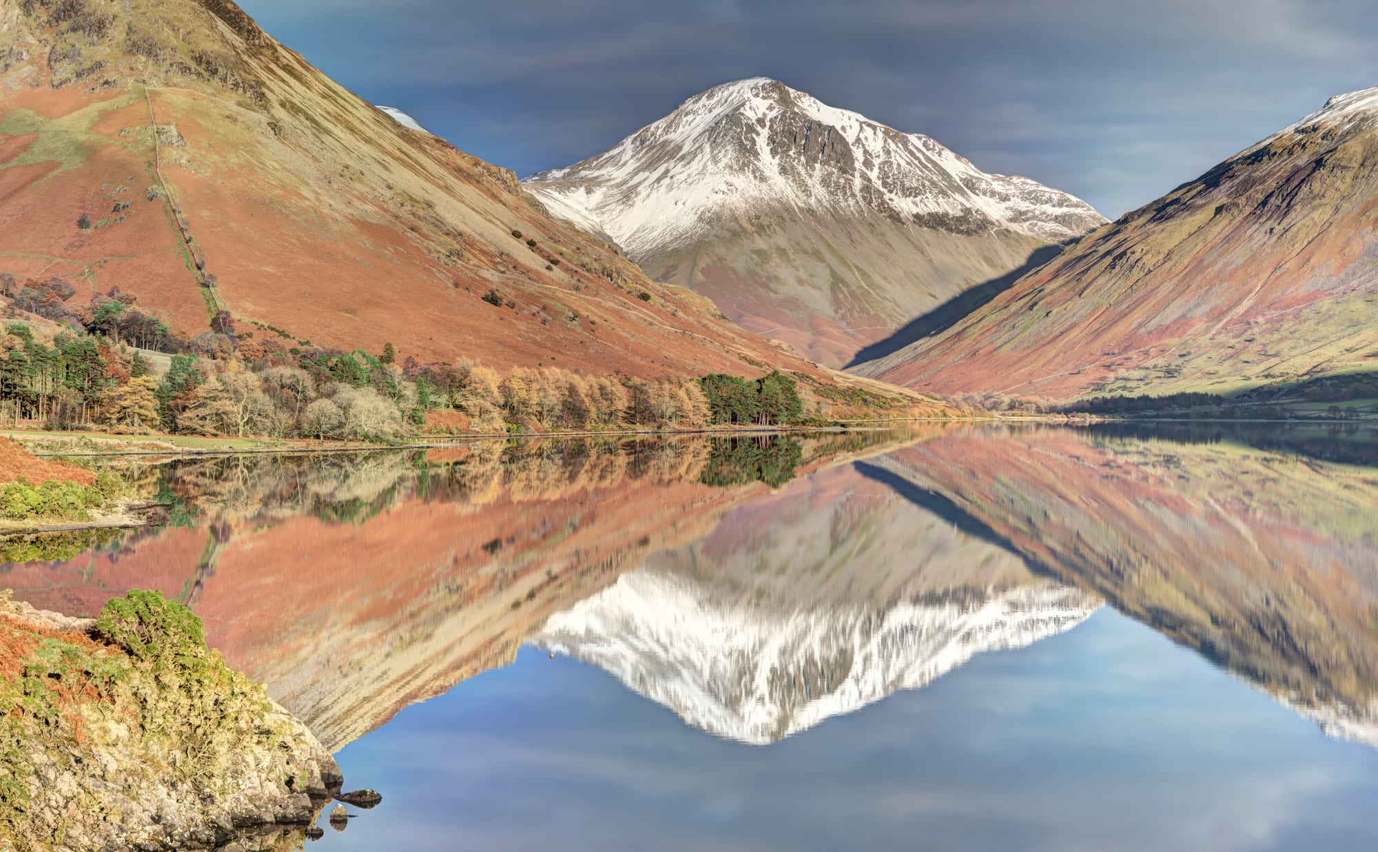 A snow-capped pyramid-shaped mountain between bracken-covered slopes, mirrored in the still water of a lake