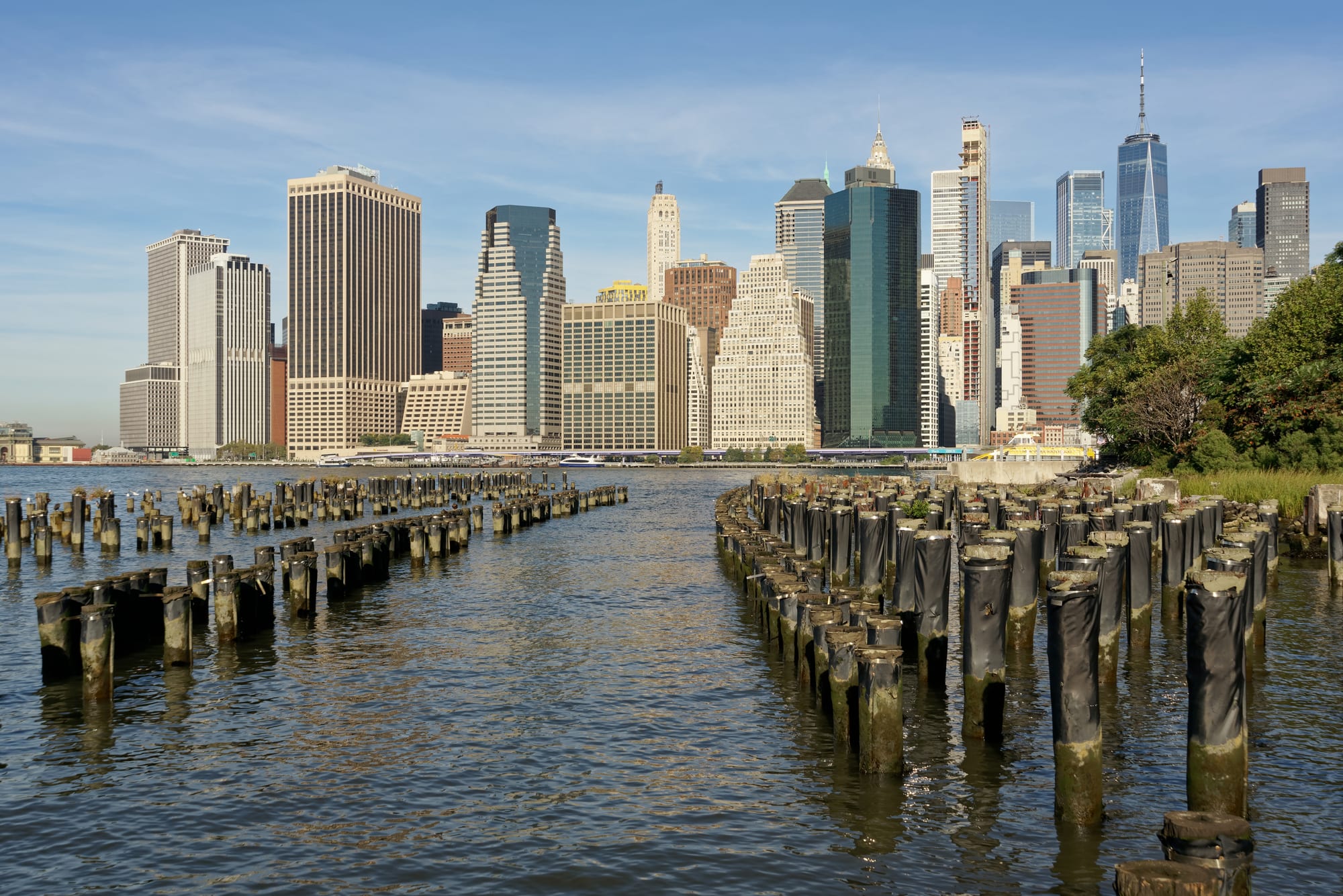 Skyscrapers of Lower Manhattan across the East River, with rows of old wooden pier posts in the water in front