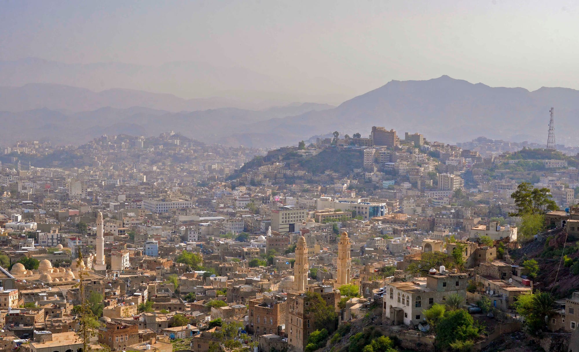 Hazy view over the low buildings of Taiz with twin white minarets in the foreground and mountains behind